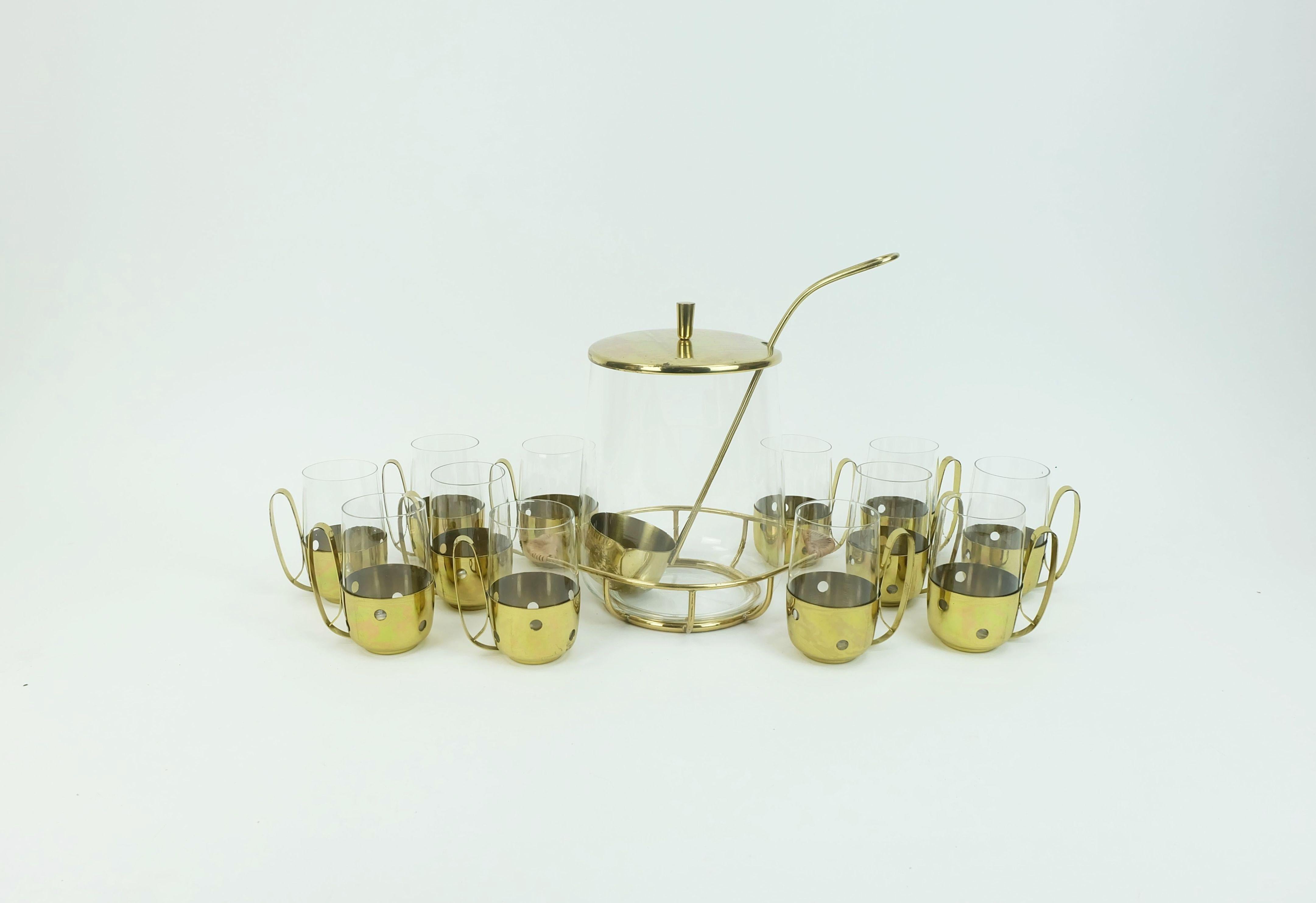 Très beau service à punch du milieu du siècle dernier, datant des années 1950. Les verres sont placés dans des supports élégants en laiton fin avec un motif de trous. Le support pour le bol à punch est également en laiton avec des poignées gainées