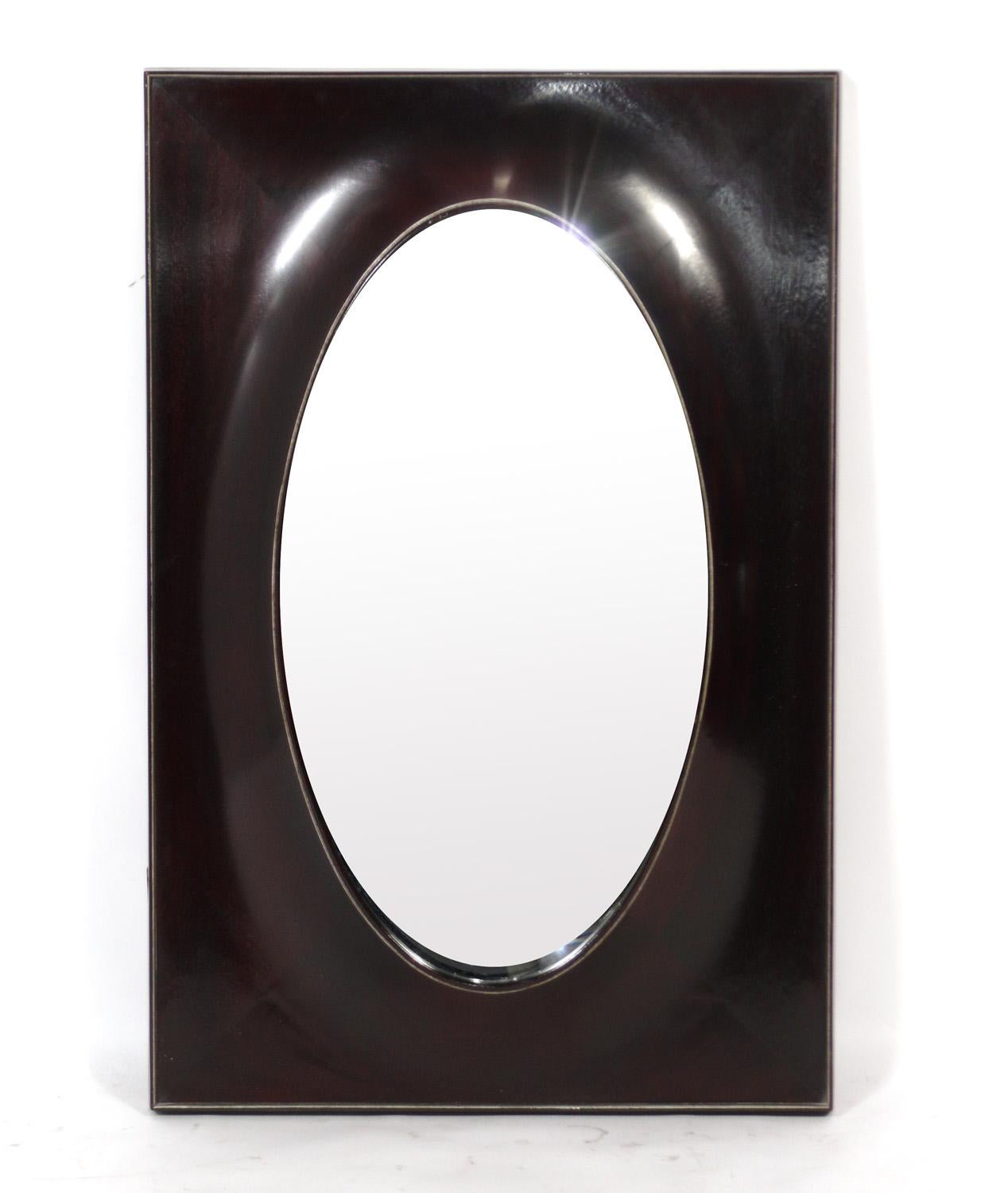 Elegant mirror, designed by Barbara Barry for Baker, American, circa 2000s. 
It is constructed of an oval mirror inset in a sculptural dark brown lacquered rectangular mahogany frame.