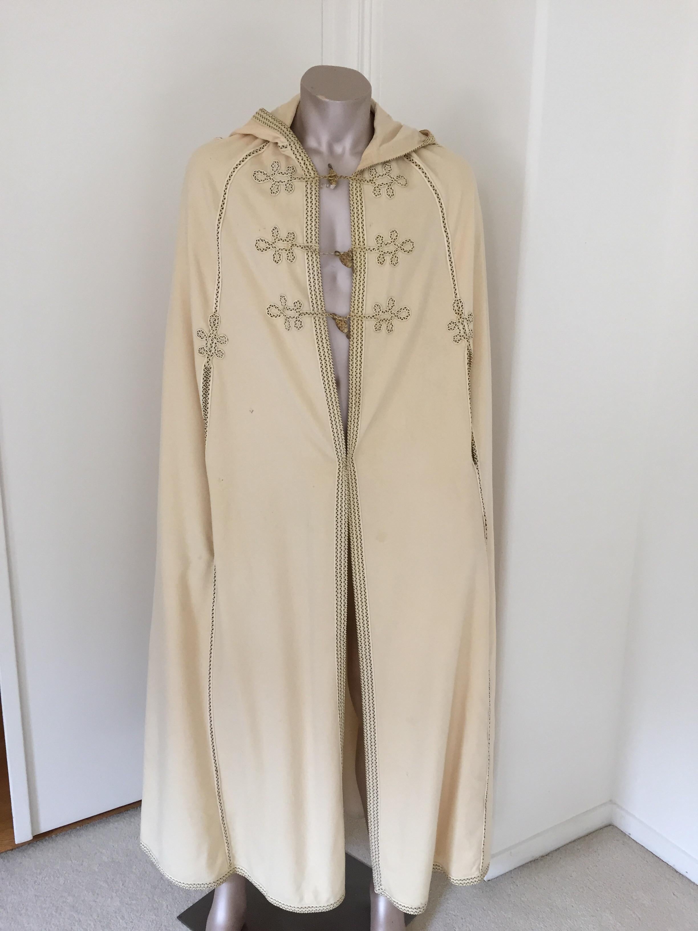 Elegant Moroccan hooded burnous cape in off-white fine wool with black and ivory passementerie trim and closure a long tassel on hood, the caftan is fully Lined.
The burnus (also called a selham) is long, hooded cloak worn in North Africa and the