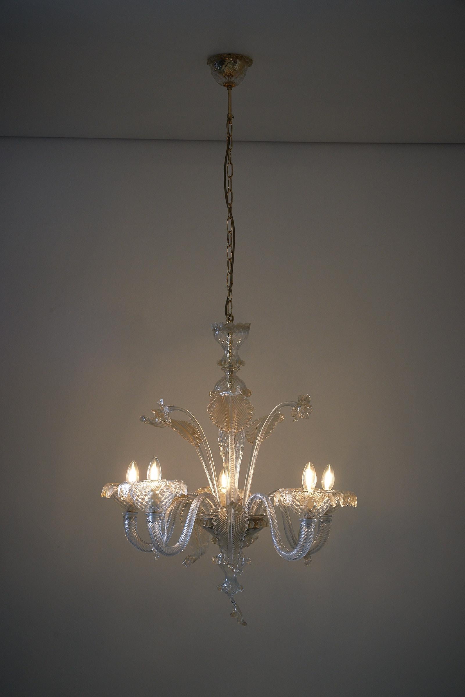 Te presentamos una impresionante lámpara de cristal de Murano adornada con cristal transparente elegantemente coloreado con oro en el interior. Esta exquisita pieza tiene cinco brazos hacia arriba y está en perfecto estado.
el candelabro viene con