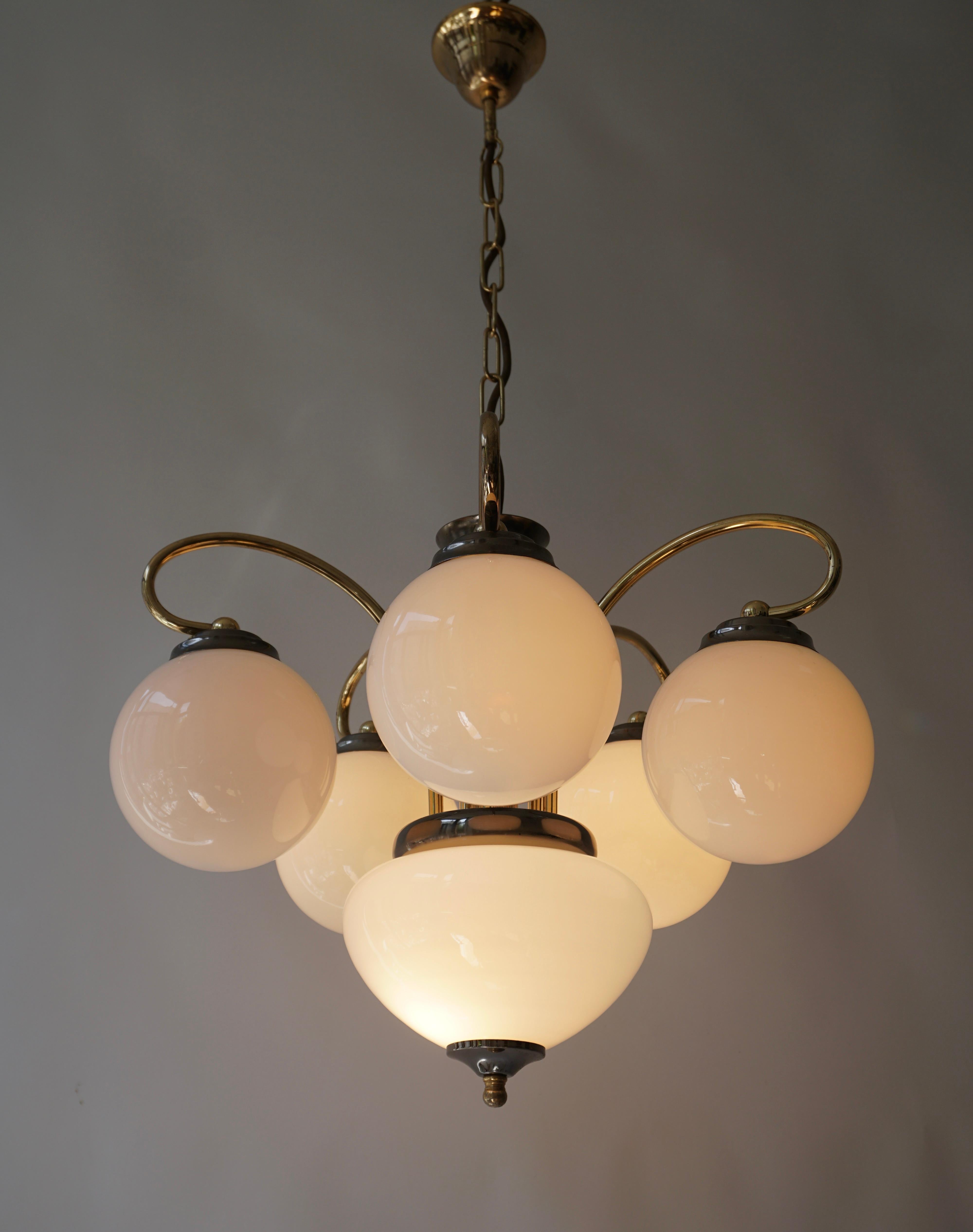 Elegant chandelier in brass and opal glass, Italy, 1970s.   

This elegant chandelier has six shades in opal glass, with a wonderful warm light spread. The tubular brass frame shows five elegantly curved mounting elements, holding the shades. All