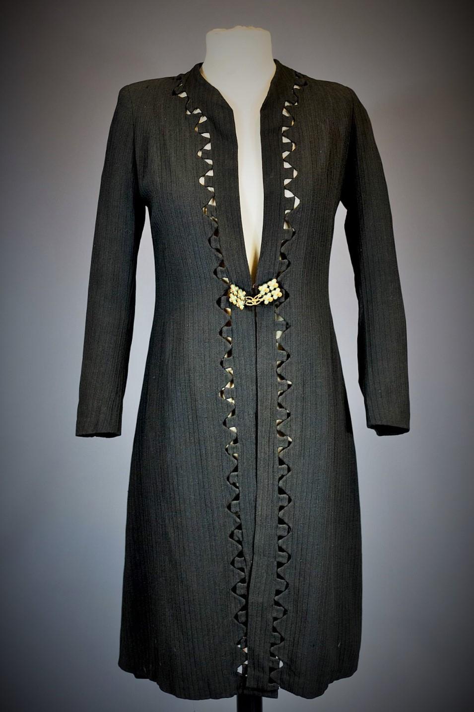 Circa 1935-1945

France

Elegant evening coat in black woollen crepe with geometric and openwork motifs around the edges, signed withl'Aigle Royal, a fashion house in Blois. Very fluid coat or dress, long sleeves and front fastening with a patent