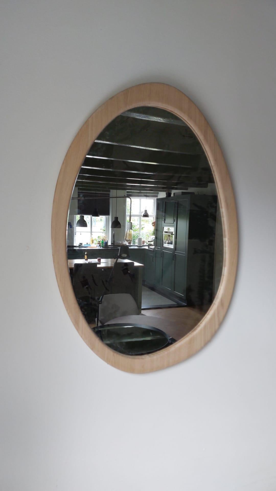 Dieser luxuriöse Wandspiegel aus Eichenholz zeichnet sich durch eine dezent organische Silhouette aus, die natürliche Eleganz und moderne Raffinesse nahtlos miteinander verbindet. Der Rahmen ist aus hochwertigem, gealtertem Eichenholz gefertigt und