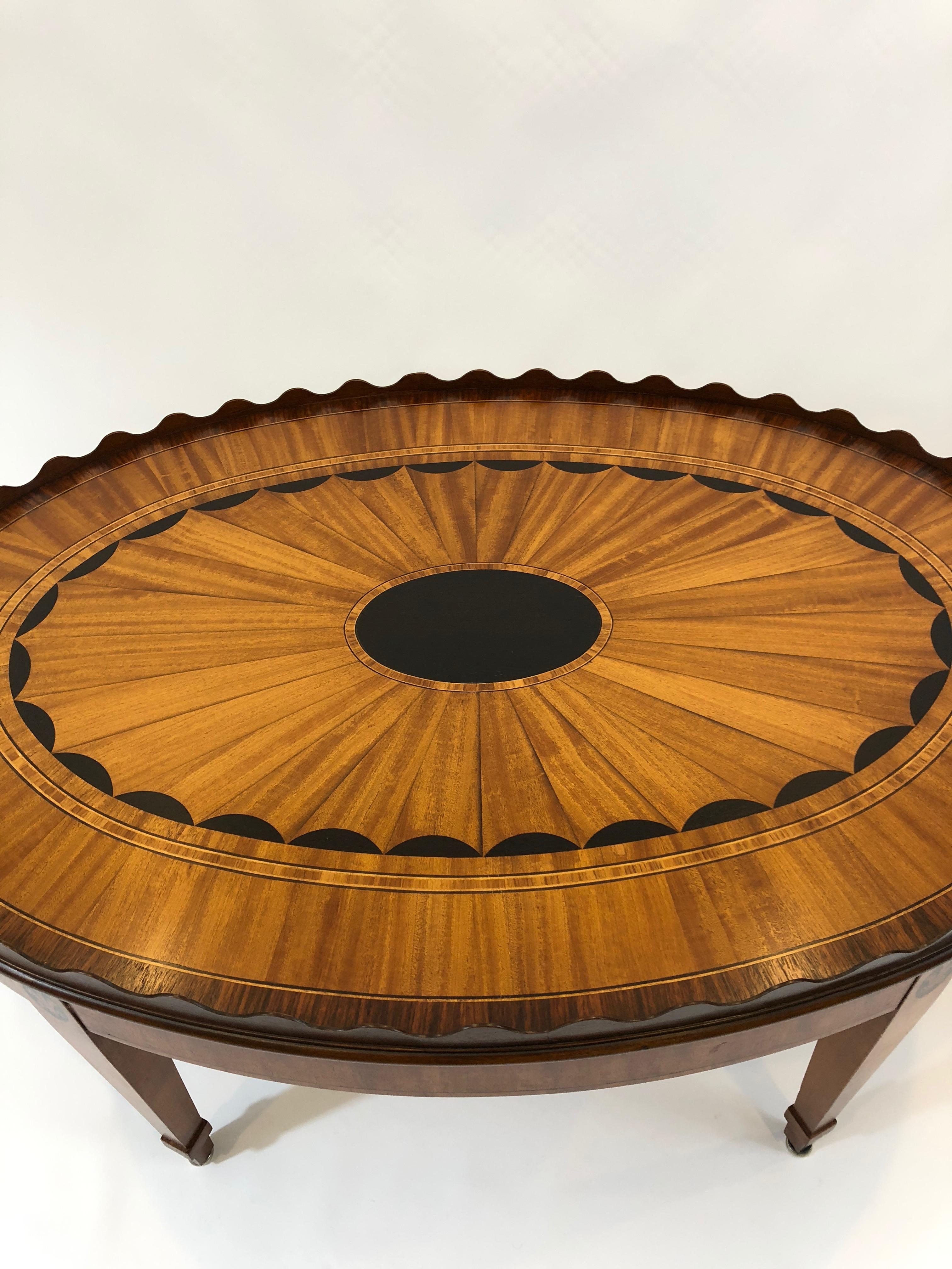 A magnificent satinwood oval cocktail table by EJ Victor having intricate ebony and rosewood veneer inlay and a pretty scalloped edge, with fleur di lis decoration on the tapered elegant legs. Fixed tray top has brass handles.