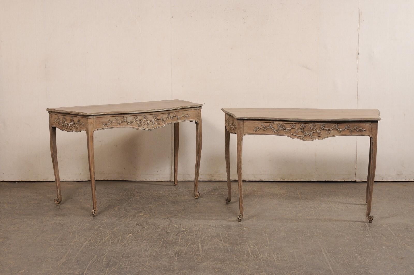 A French pair of nicely-sized wooden console tables, with beautifully embellished aprons, from the 19th century. This antique pair of tables from France have a soft and shapely serpentine design along their front and sides, with their flatter