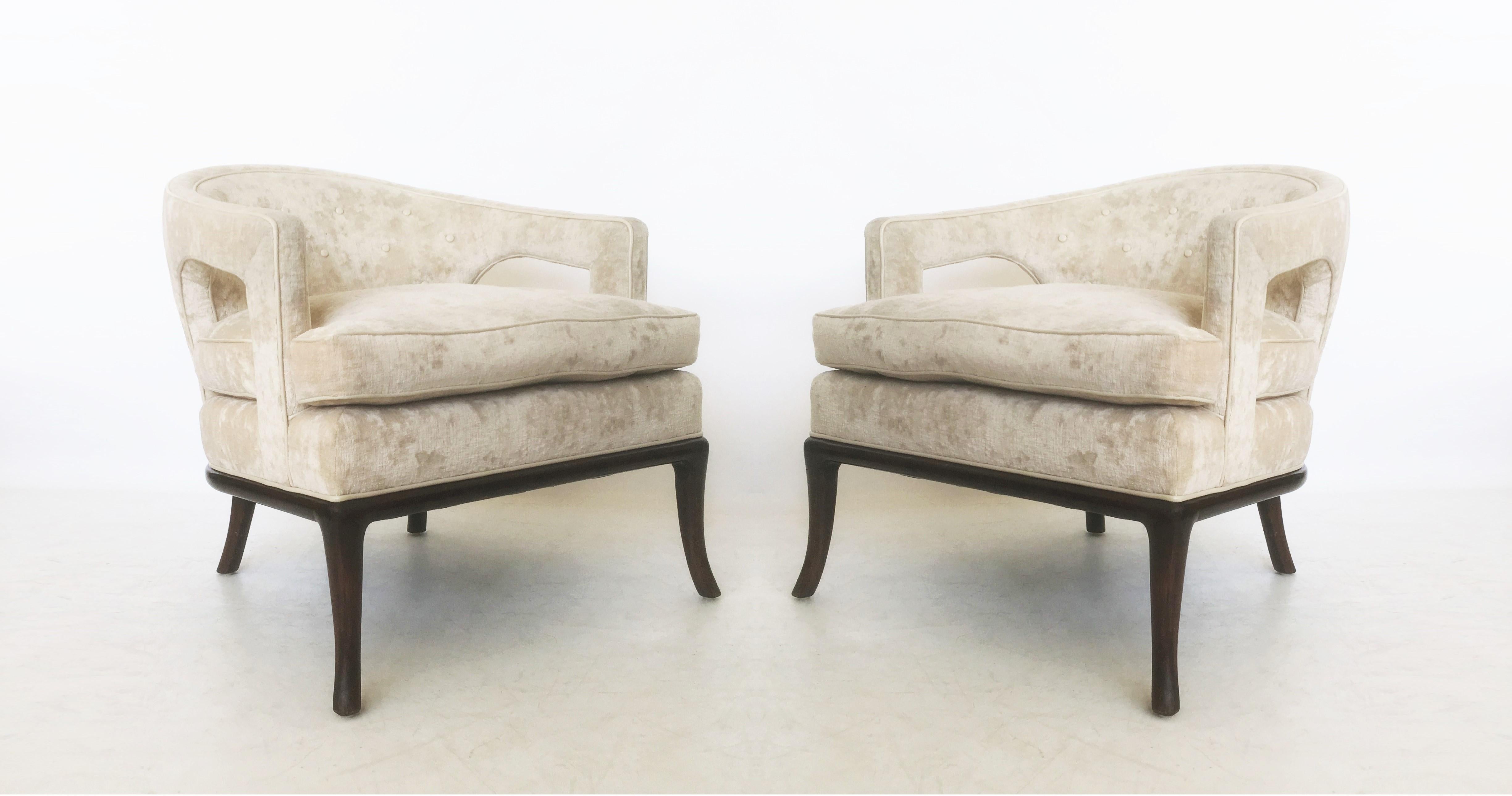 Pair of upholstered club chairs by T.H. Robsjohn-Gibbings for Widdicomb, American, 1950s. The chairs feature barrel-backs with cut-out arms and sculpted legs. Upholstered in a cream colored velvet, features a leather button-tufted back and leather