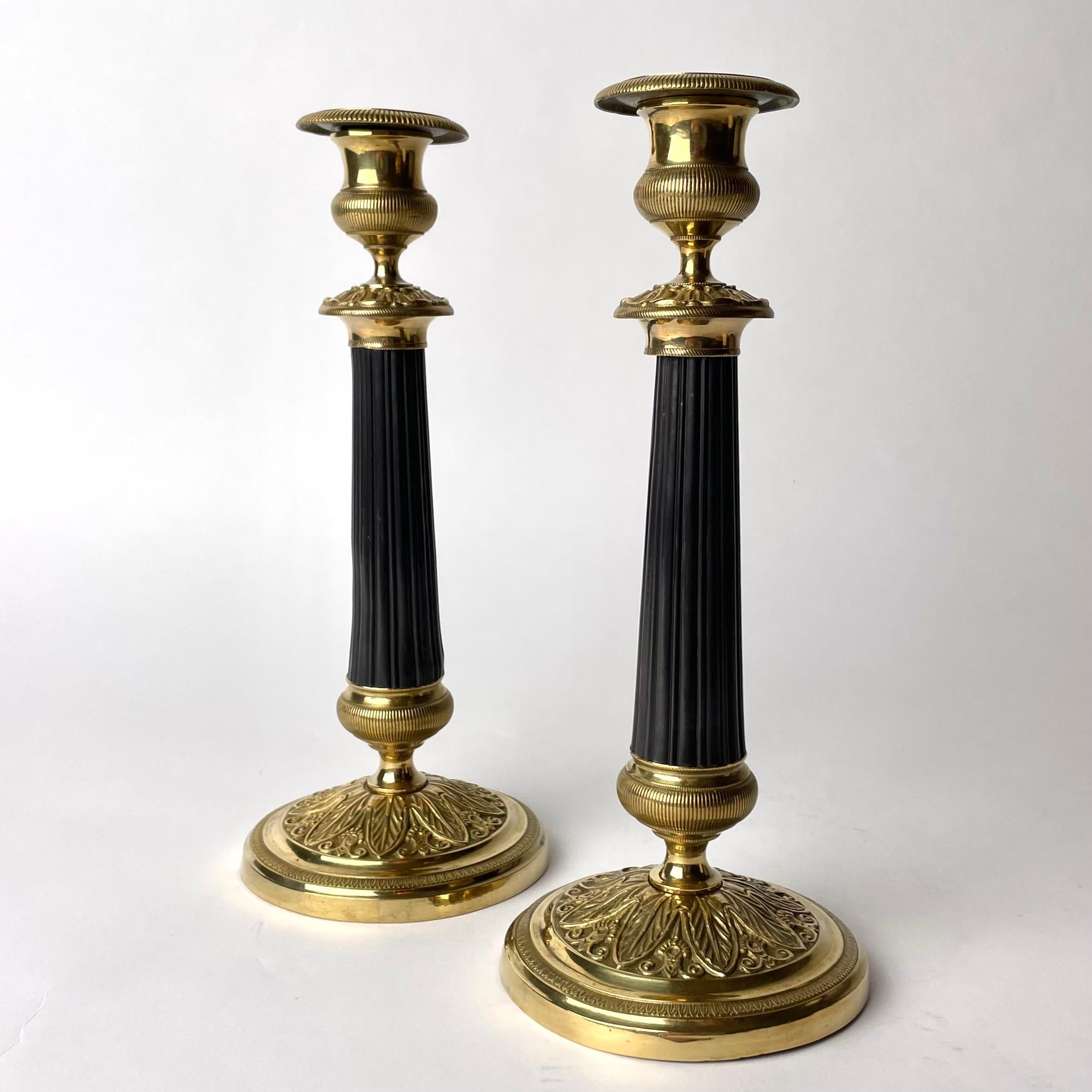Elegantes Paar Kerzenleuchter aus vergoldeter und dunkel patinierter Bronze im Empire-Stil.  Hergestellt in Frankreich in den 1920er Jahren. Schön verziert mit Blattornamenten und mit einer dunkel patinierten Säule in der Mitte des