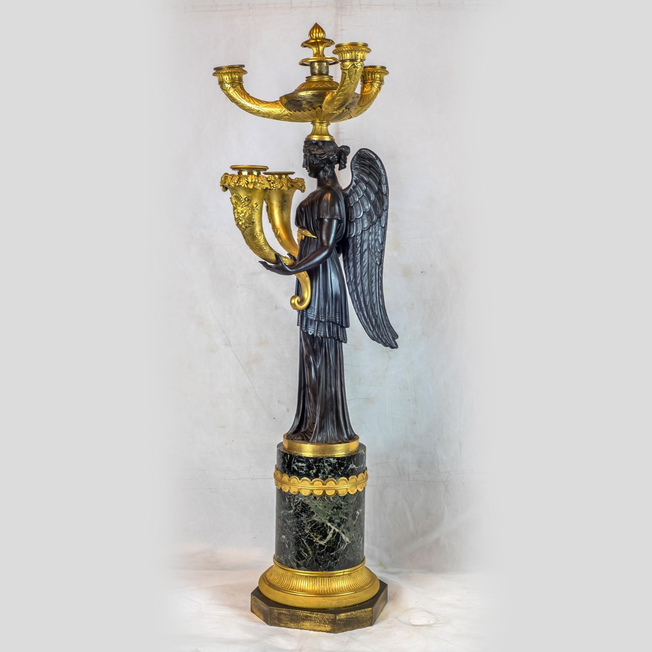 An Elegant pair of Empire Patinated and gilt bronze five-light candelabras. 
Each candelabra formed as a winged maiden holding a cornucopia torch in each hand, surmounted on vert de mer marble bases. 

Date: circa 1810
Origin: French
Dimension: