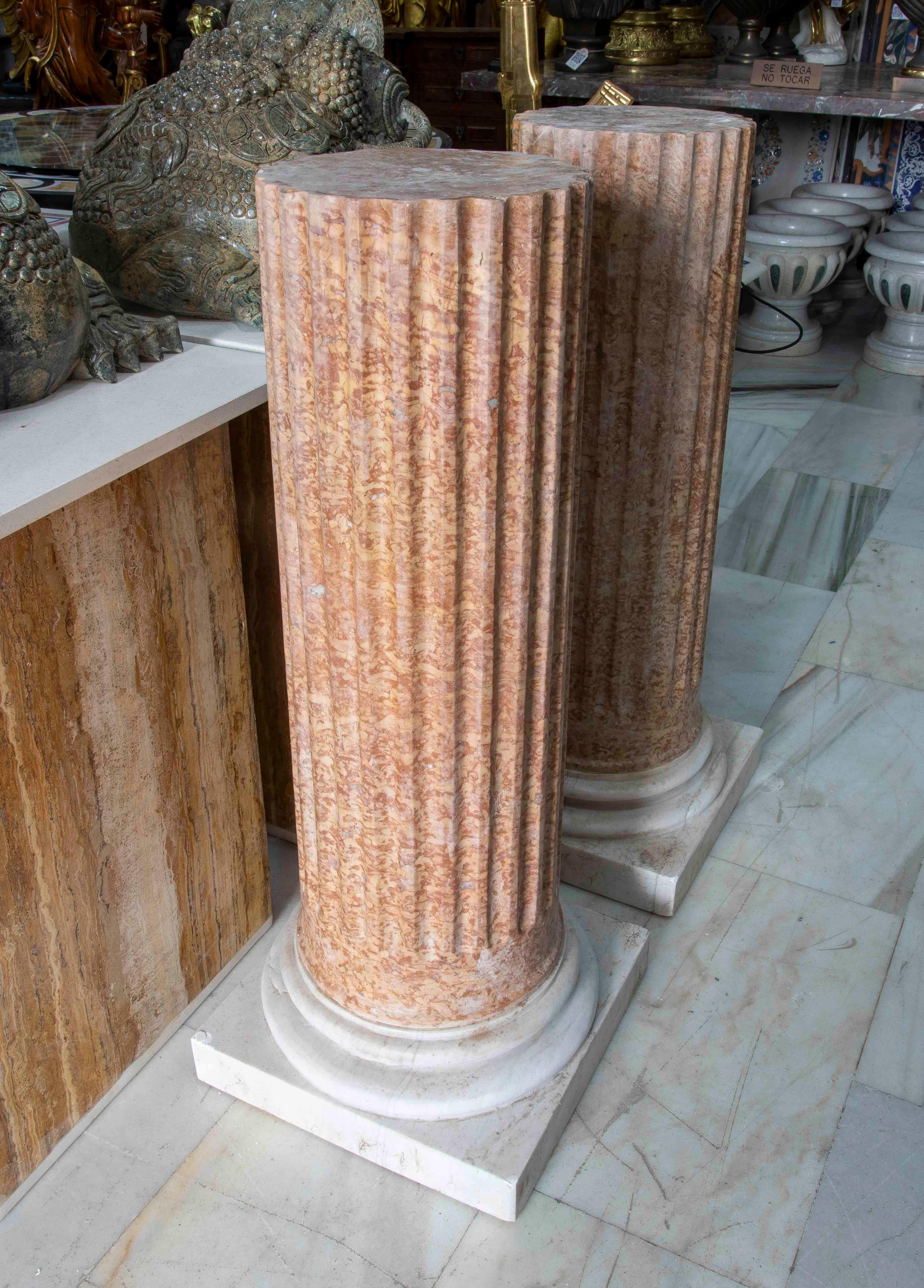 Ein beeindruckendes Paar klassischer Sockel aus natürlich geädertem rotem Marmor, die auf massiven weißen Marmorsockeln stehen. Jedes Stück weist ein elegantes Streifendesign auf, das Textur und Tiefe verleiht und an antike Architektur erinnert.