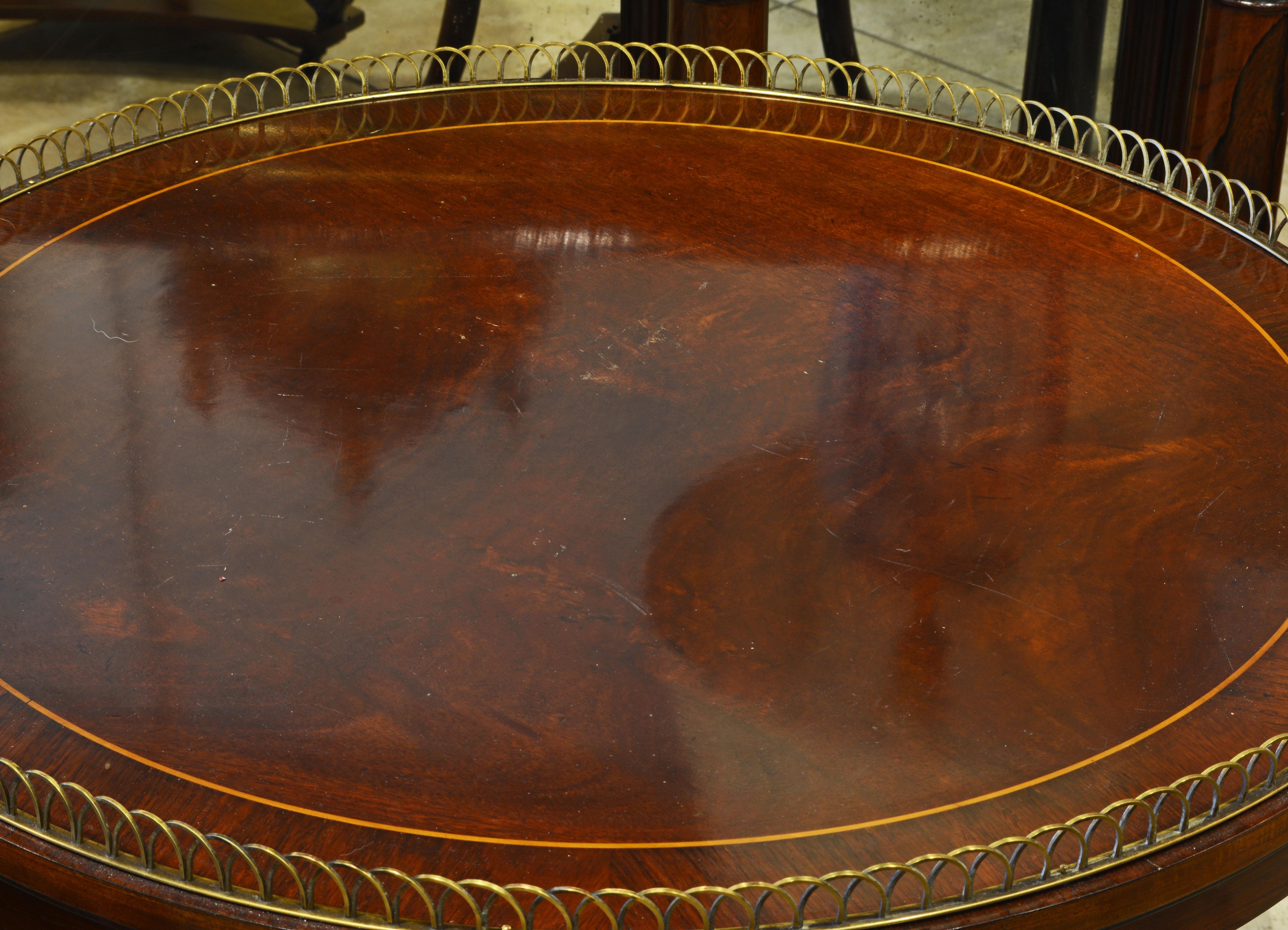 This fine pair of French Directoire style tables feature rosewood banded mahogany tops edged by circle segment bronze galleries and supported by three curved legs carved with scrolls united by a second tier gallery shelf and resting on a shaped