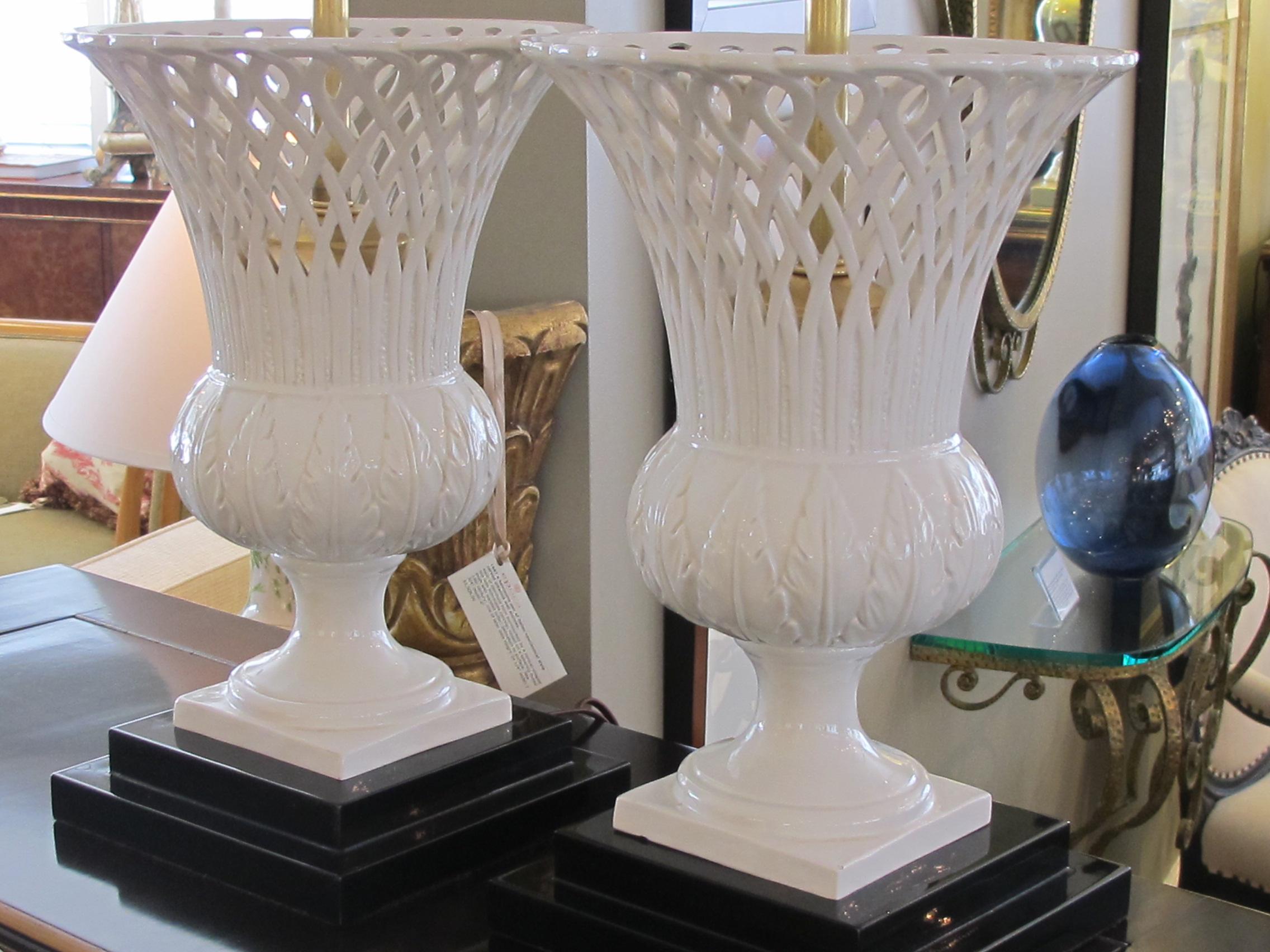 A stylish pair of Italian white-glazed urns with over-scaled flared reticulated neck over a bulbous mid-section with raised foliate decoration; raised on a splayed base resting on a black lacquer wooden plinth; 16