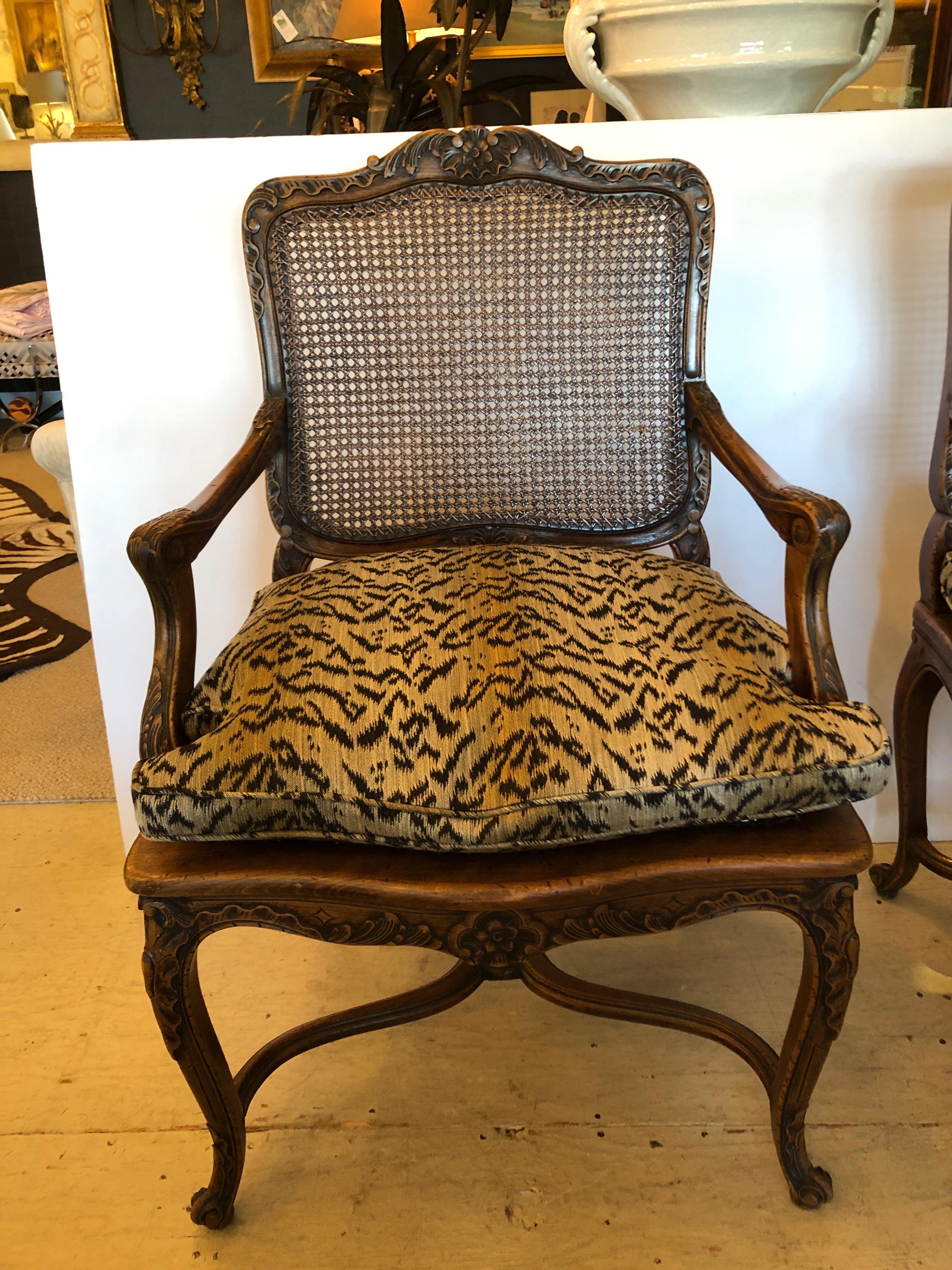 Rich looking carved walnut Regence French armchairs having lovely decoration, pristine caned backs and seats, cabriole legs, and faux tiger cushions stuffed with comfortable down.