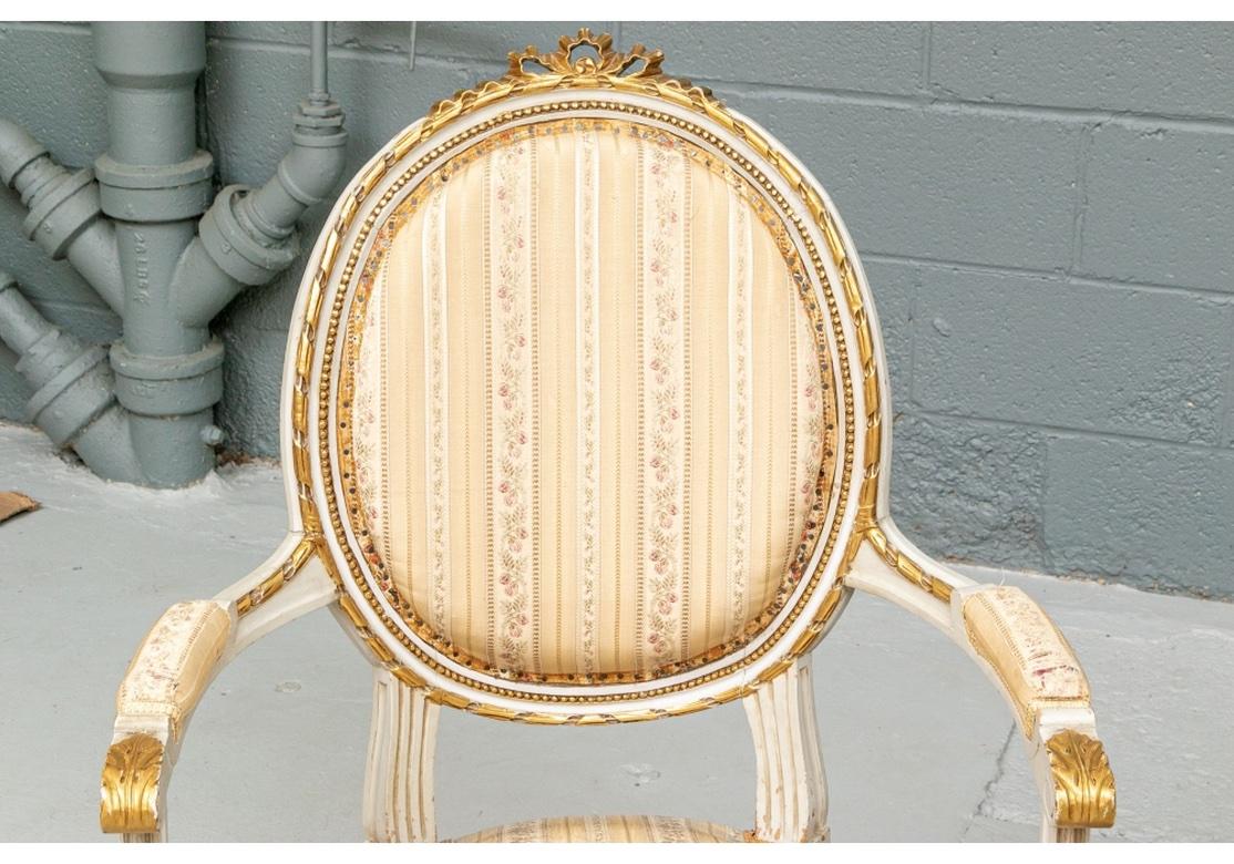 Finely constructed Louis XVI style fauteuils in pale gray paint with gilt details. The oval backs with gilt ribbon twist outer frames, ribbon bow crests and beaded inner frames. The arms with gilt acanthus leaf ends and arm supports. The seat rail