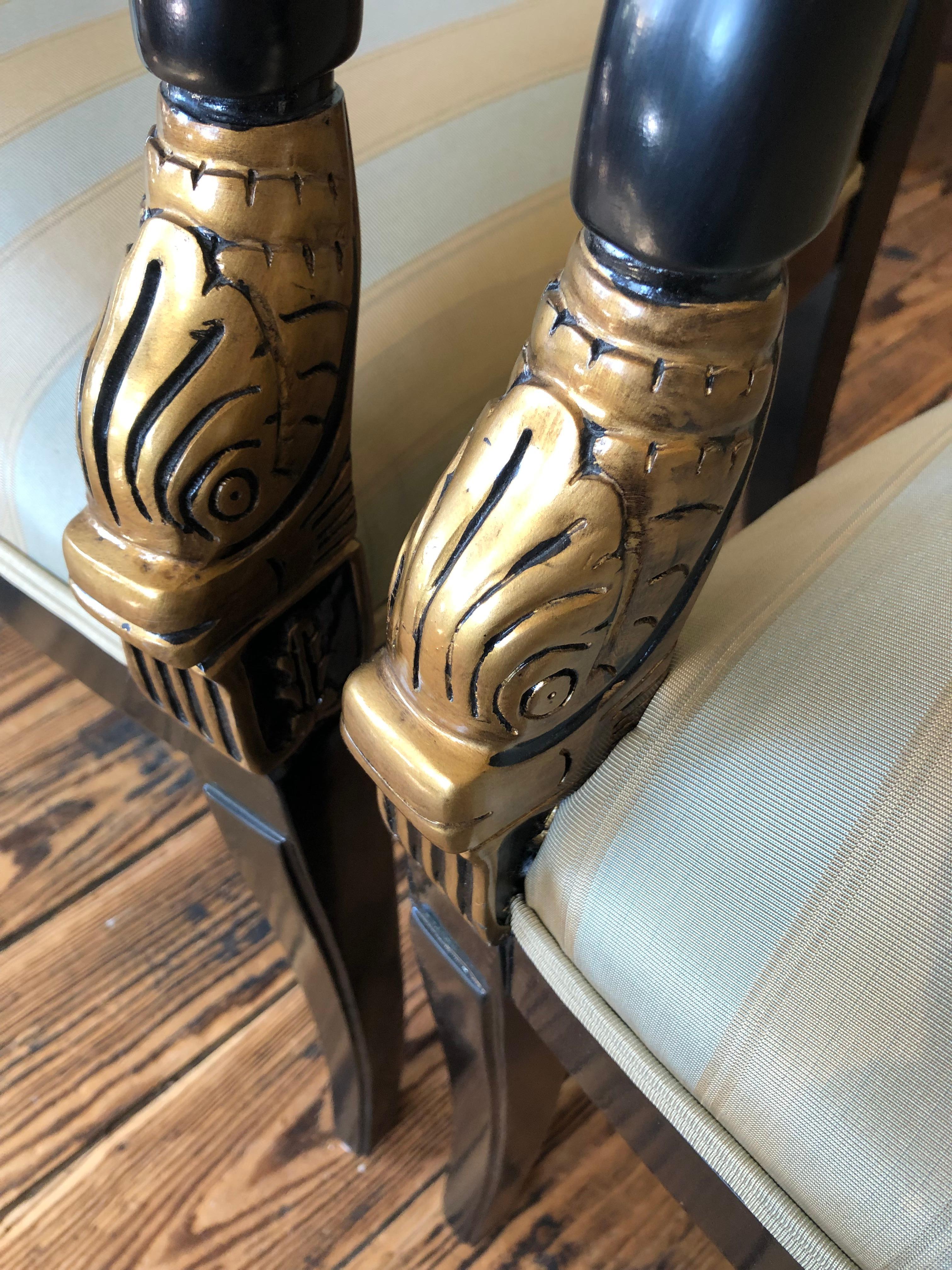 Magnifique paire de fauteuils de style Regency, avec des cadres noirs et des motifs de dauphins dorés sur les accoudoirs et une tapisserie d'ameublement neutre. Hauteur des bras 25,5