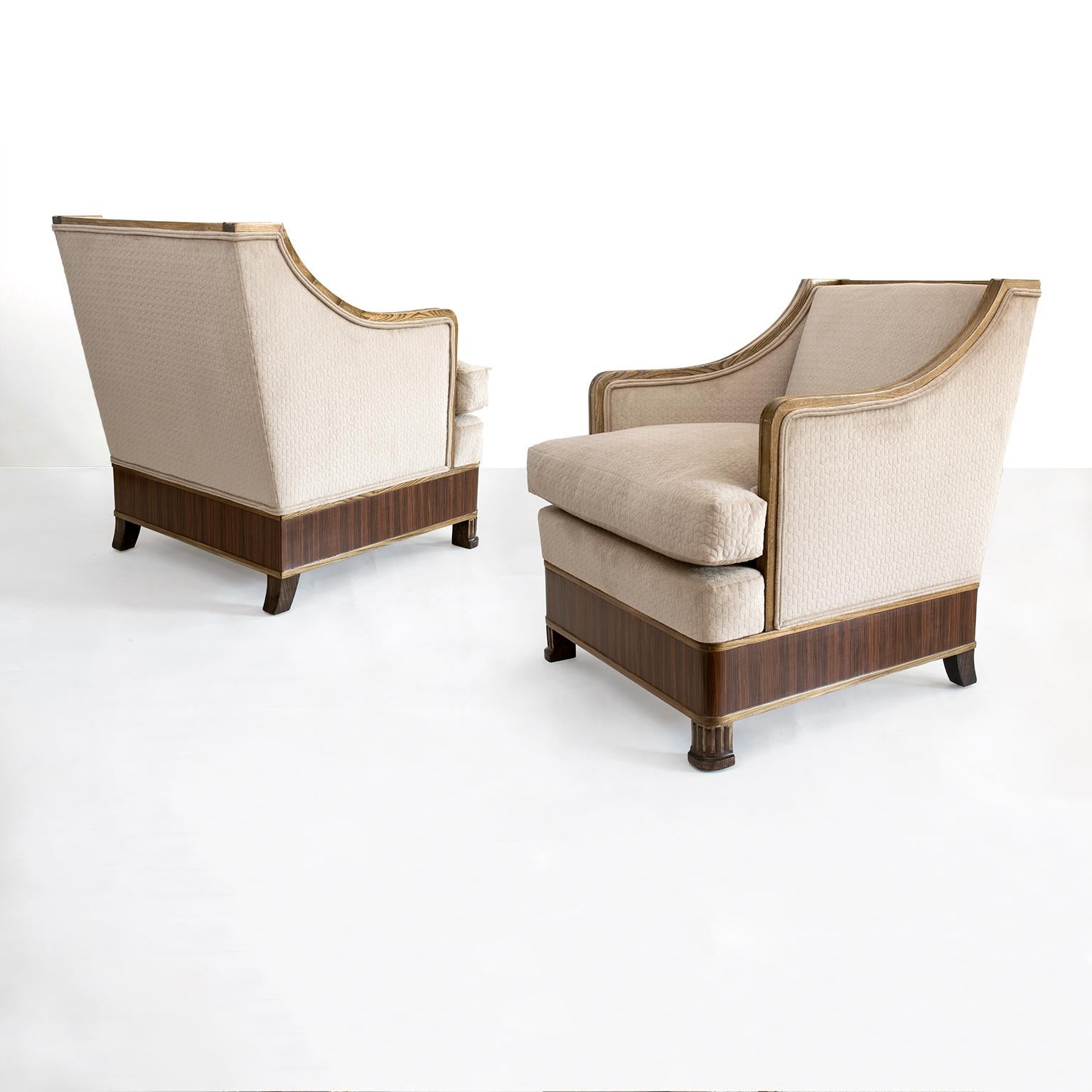 A roomy, stylish and very comfortable pair of Swedish Art Deco upholstered armchairs. Frames are carved solid elmwood with front legs in the form of a columns and a band of mahogany veneer wraps around each chair's base. Newly restored and newly