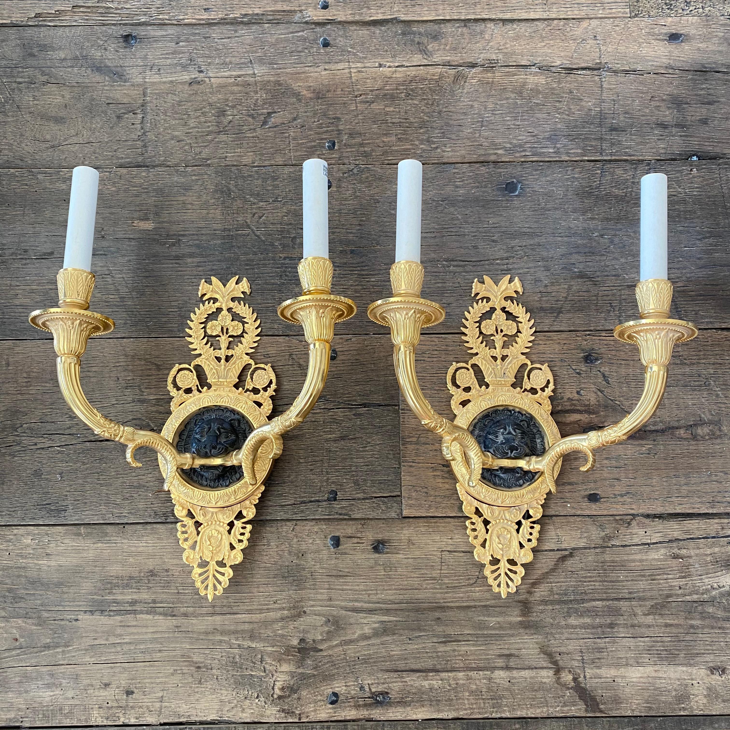 Distinguished pair of Empire style, French brass sconces having intricate detail on the two shaped arms. The lion heads sit on a black enameled, circular base. The pie`ce de re´sistance to your classical decor; perfect in a library or a formal