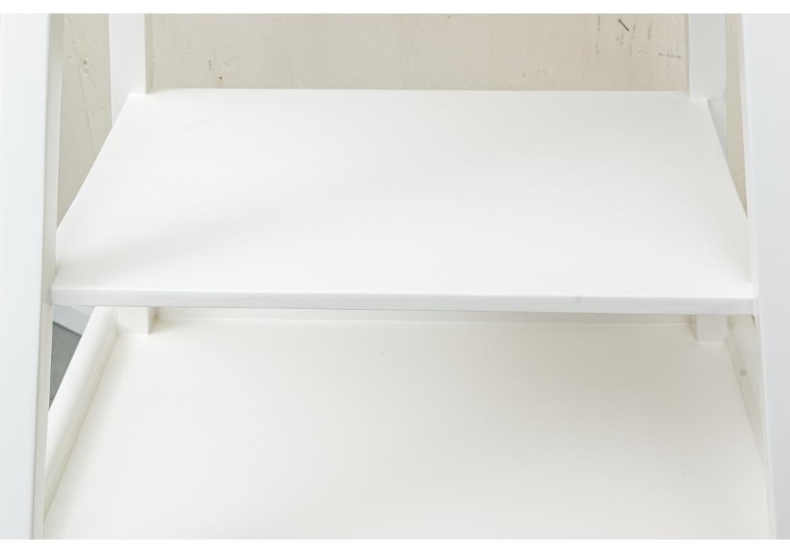 Pareja de etageras decoradas con pintura blanca y rematadas en forma piramidal sobre una base rectangular. Ambos en una sola pieza, con tres estantes inferiores escalonados, sobre cuatro patas cuadradas, la parte superior con galería corta. La parte