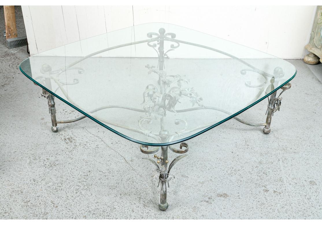 A large and very decorative Foliate Cocktail Table comprised of a scrolling frame conjoined with C-scroll motifs that support a beveled nearly square glass top. The center of the table adorned with tole leafy vines and berries terminating from a