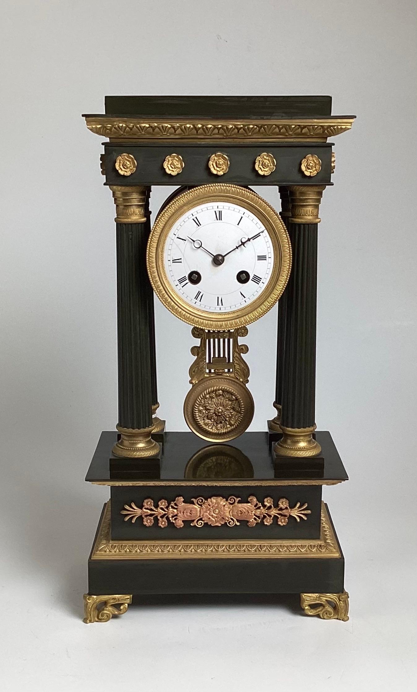 An elegant neoclassical bronze portico clock.  The patinated bronze with gilt bronze accents with round white porcelain dial.  The four columns on each side with a plinth base at the bottom.  The clock strikes at the hour and half hour, a soft crisp