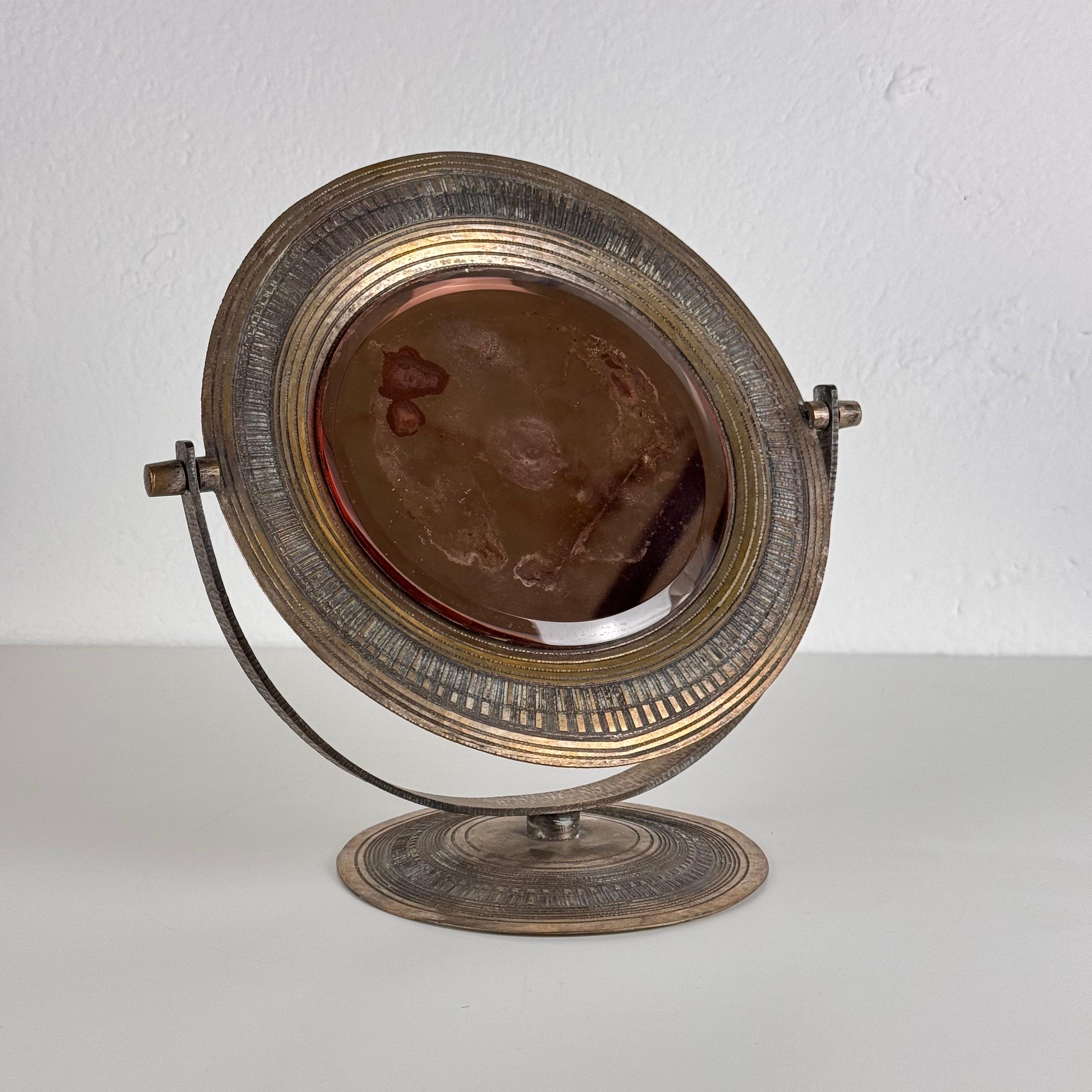 Uno squisito specchio da tavolo del rinomato scultore Celestino Gallinaro, maestro della scuola padovana, realizzato negli anni Cinquanta. Questo delicato pezzo presenta una cornice in ottone martellato e decorato a mano, che mette in mostra