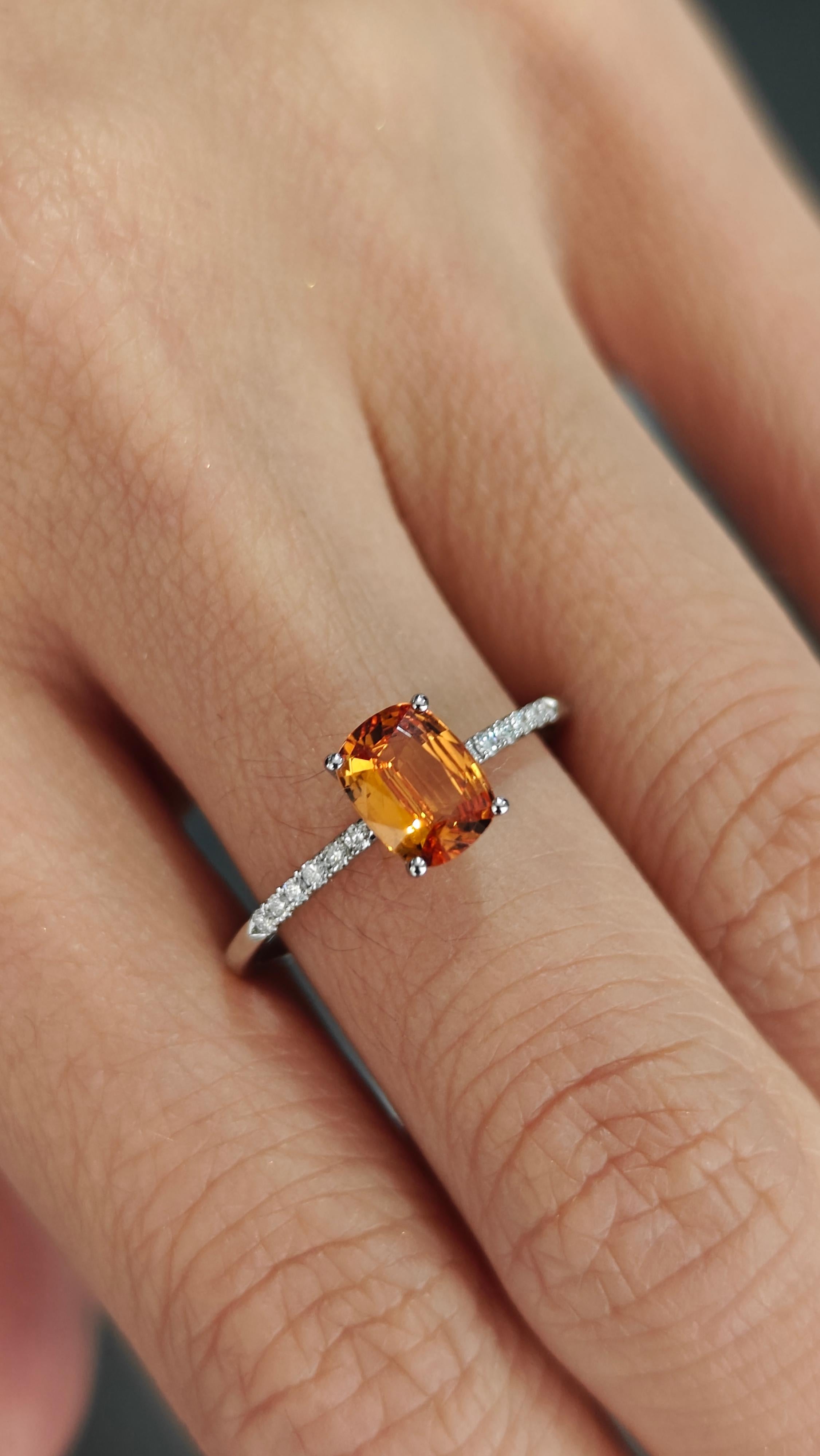 This exquisite platinum ring showcases an exceptional cushion-cut spessartite garnet as its focal point. The vibrant, fiery orange hue of the garnet radiates warmth, capturing the essence of elegance and sophistication. Complementing this stunning