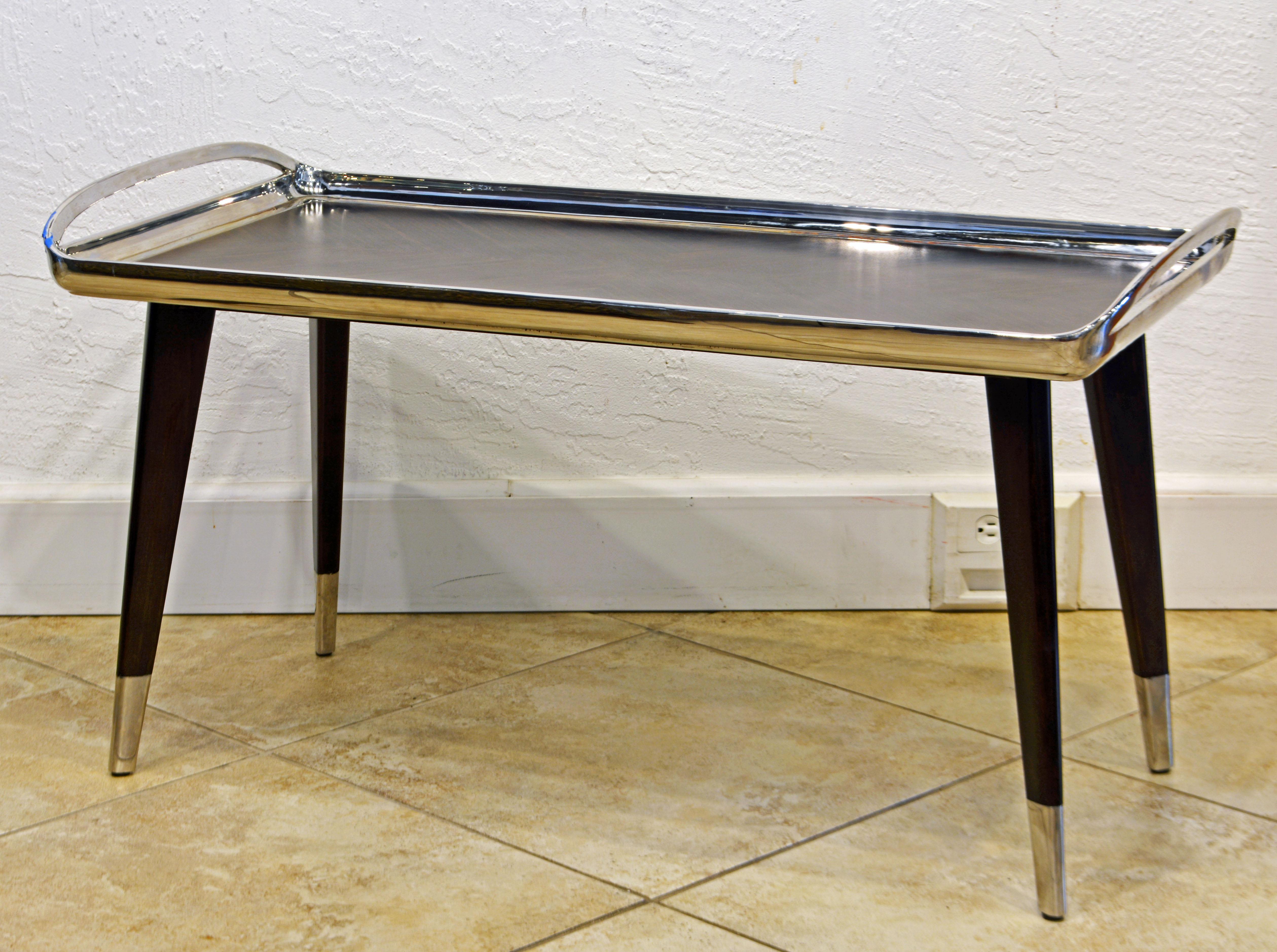 This vintage high end cocktail table by Theodore Alexander/Keno Bros. is a strikingly successful design combining a smoothly forged polished stainless frame with handles enclosing a Macassar Ebony striped parquetry table surface and creating a