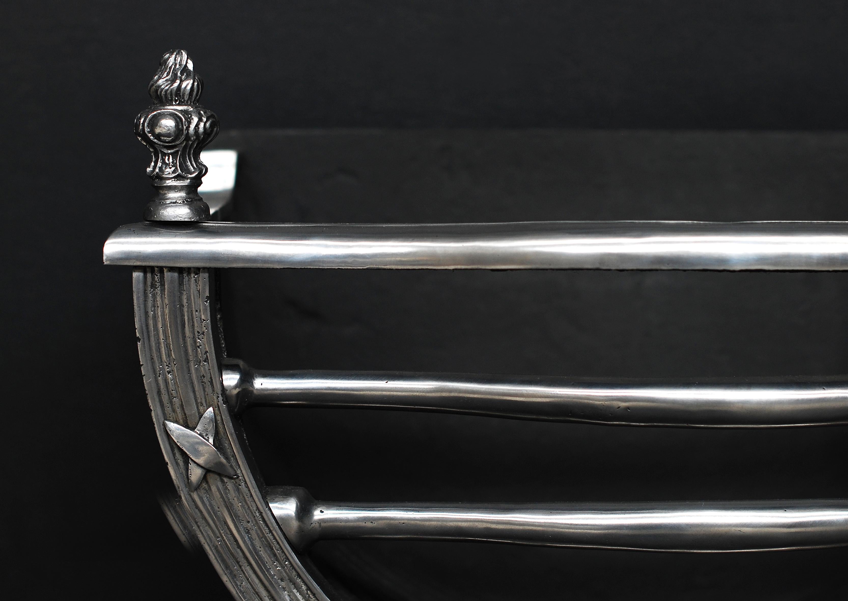A most elegant Regency style polished iron fire grate of arched form, with reeded front overlaid with steel cross band ribbons. Steel centre patera with leaf and claw feet, and flame finials.


Measures: 
Width At Front:	560 mm      	22 in
Width At