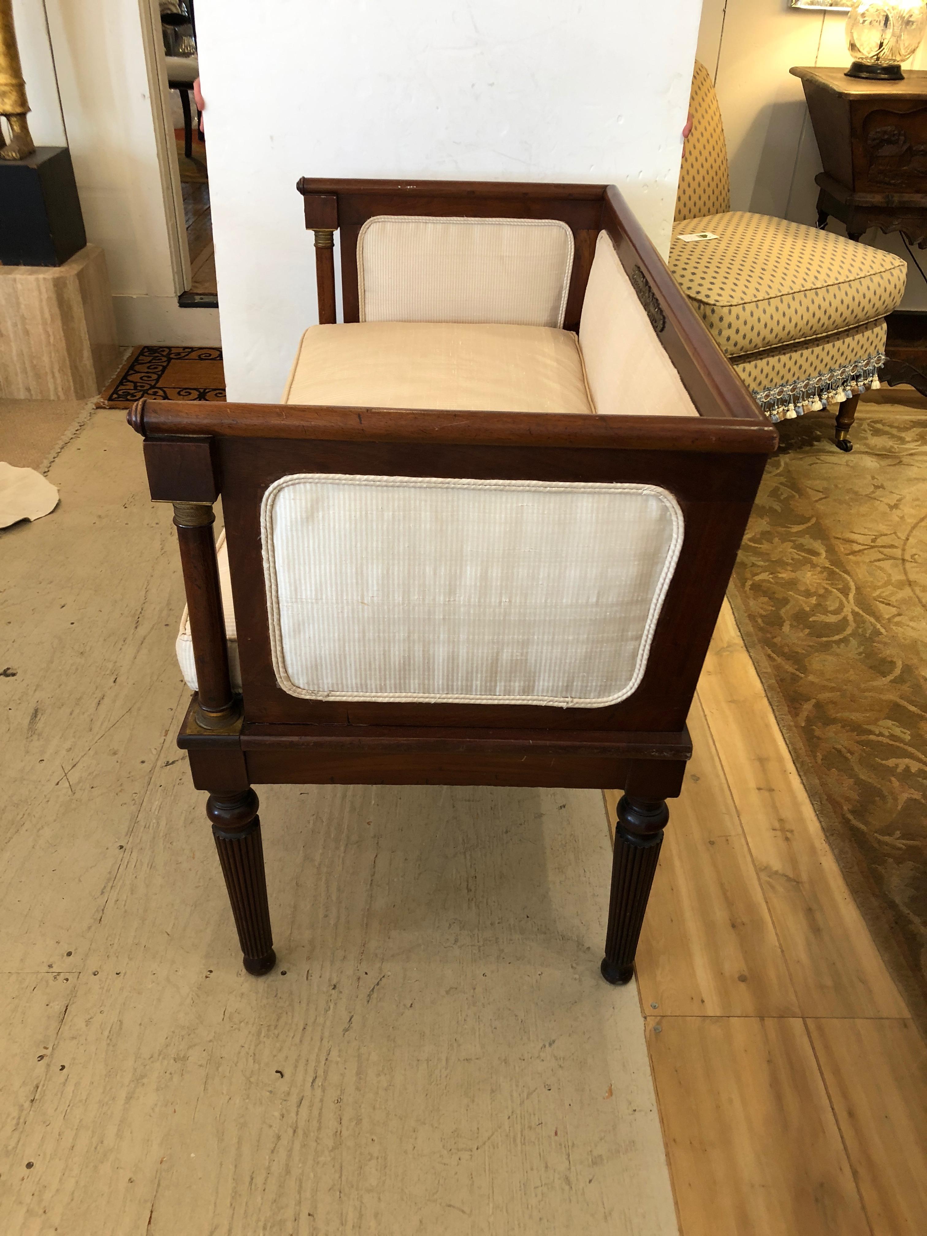 Lovely French Regency settee having upholstered frame and removable down seat cushion, pretty walnut colored mahogany frame with reeded legs and decorative brass on the top of the back and arms.
