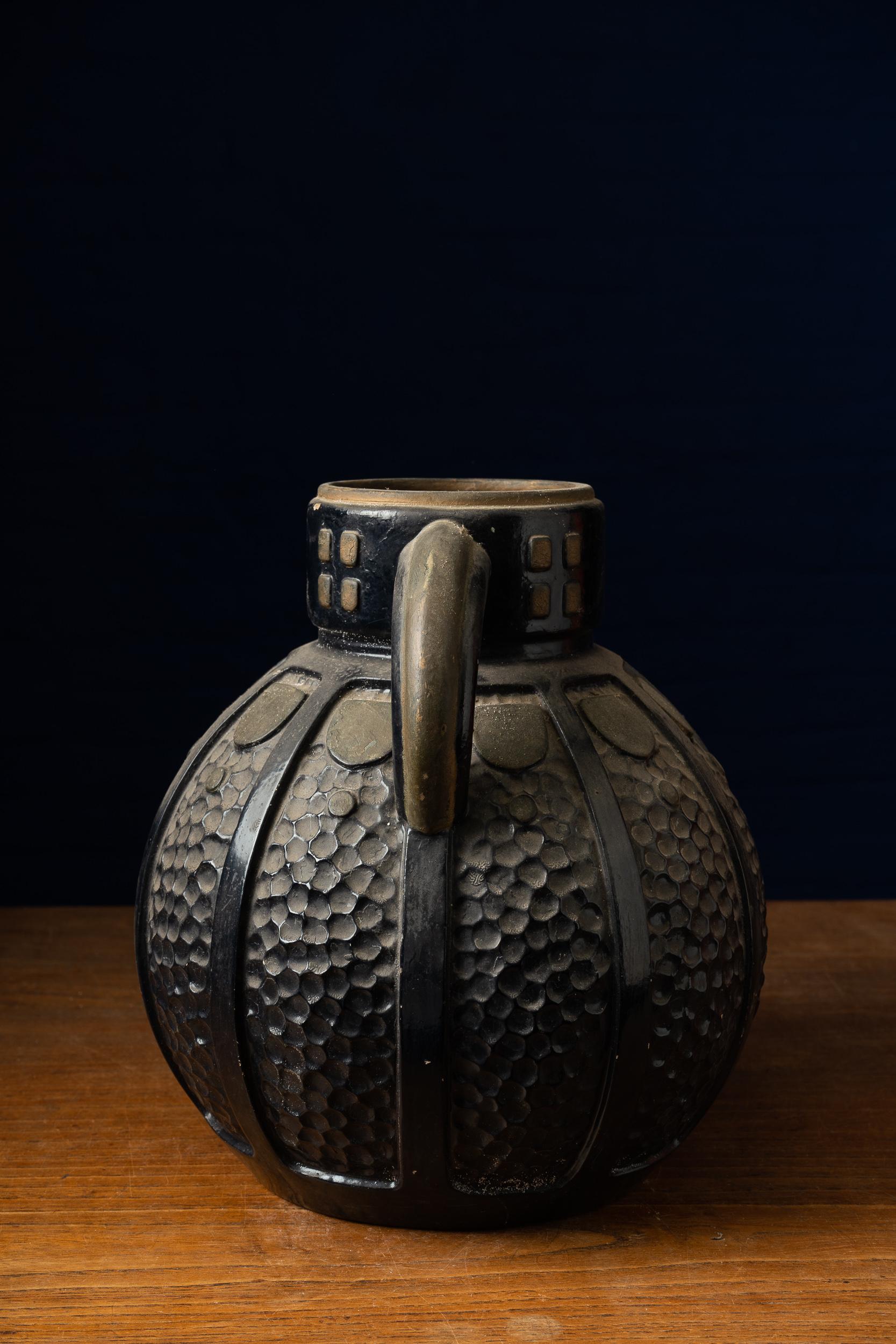 Decorative ceramics vase with a slightly patined black glaze finish and small ochre details. The item has a beautiful alveolar embossing and simple geometric shapes, as well as two holders.