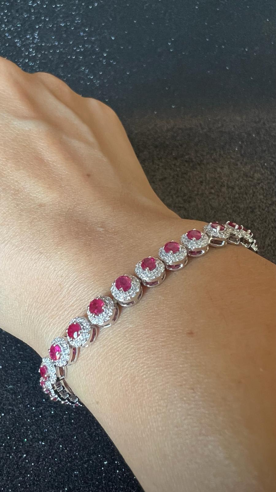 Dieses zeitlos schöne, handgefertigte Tennisarmband aus 18-karätigem Weißgold besticht durch seine lebhaften runden Rubine, die jeweils von einem zarten Halo aus funkelnden Diamanten umgeben sind. Die elegante Fassung verleiht jeder Bewegung Glanz