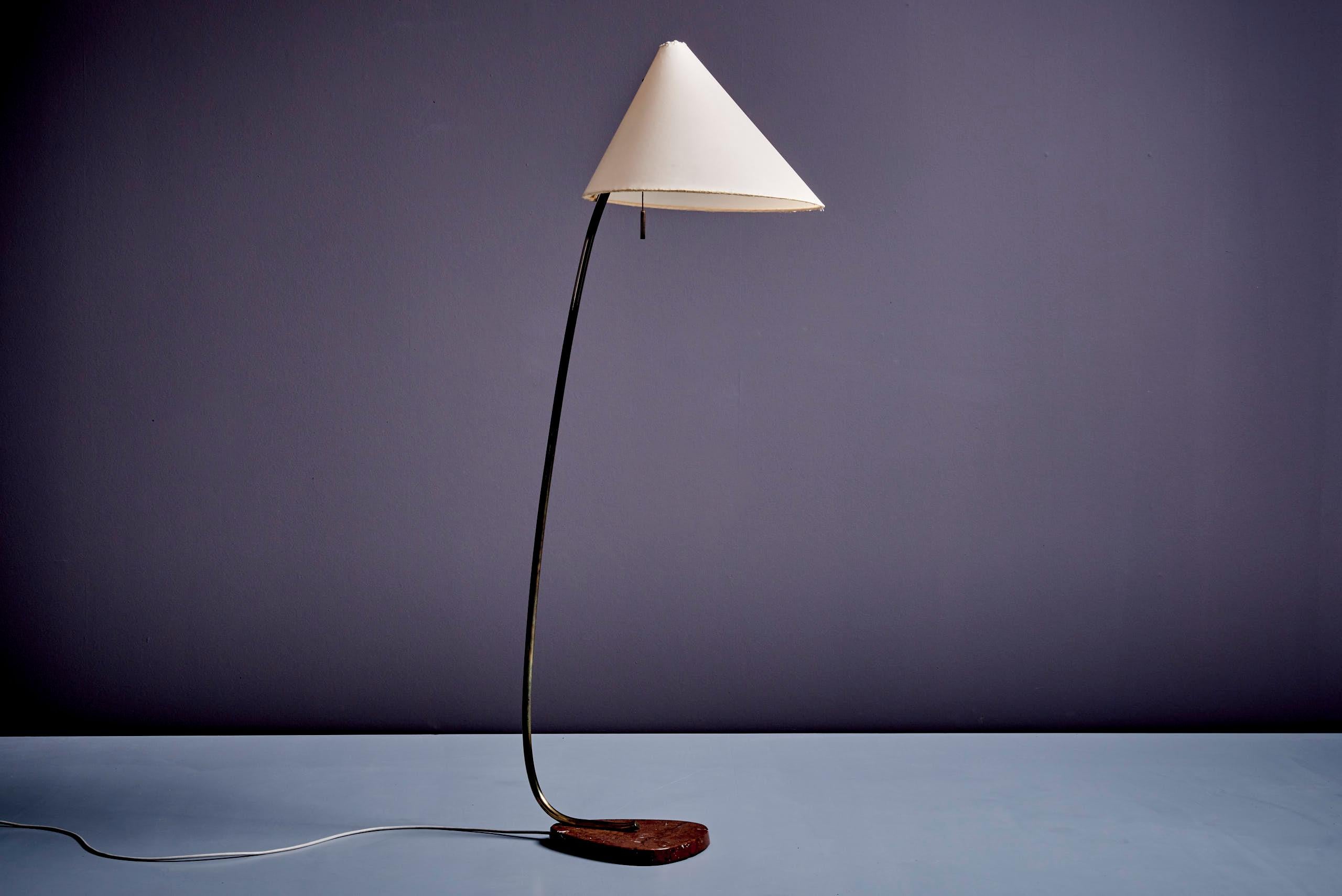 This 1950s floor lamp by Rupert Nikoll combines simplicity and elegance. The lamp features a curved brass stem and a conical fabric shade that provides soft, warm lighting. The base is made of solid marble, offering both durability and a refined