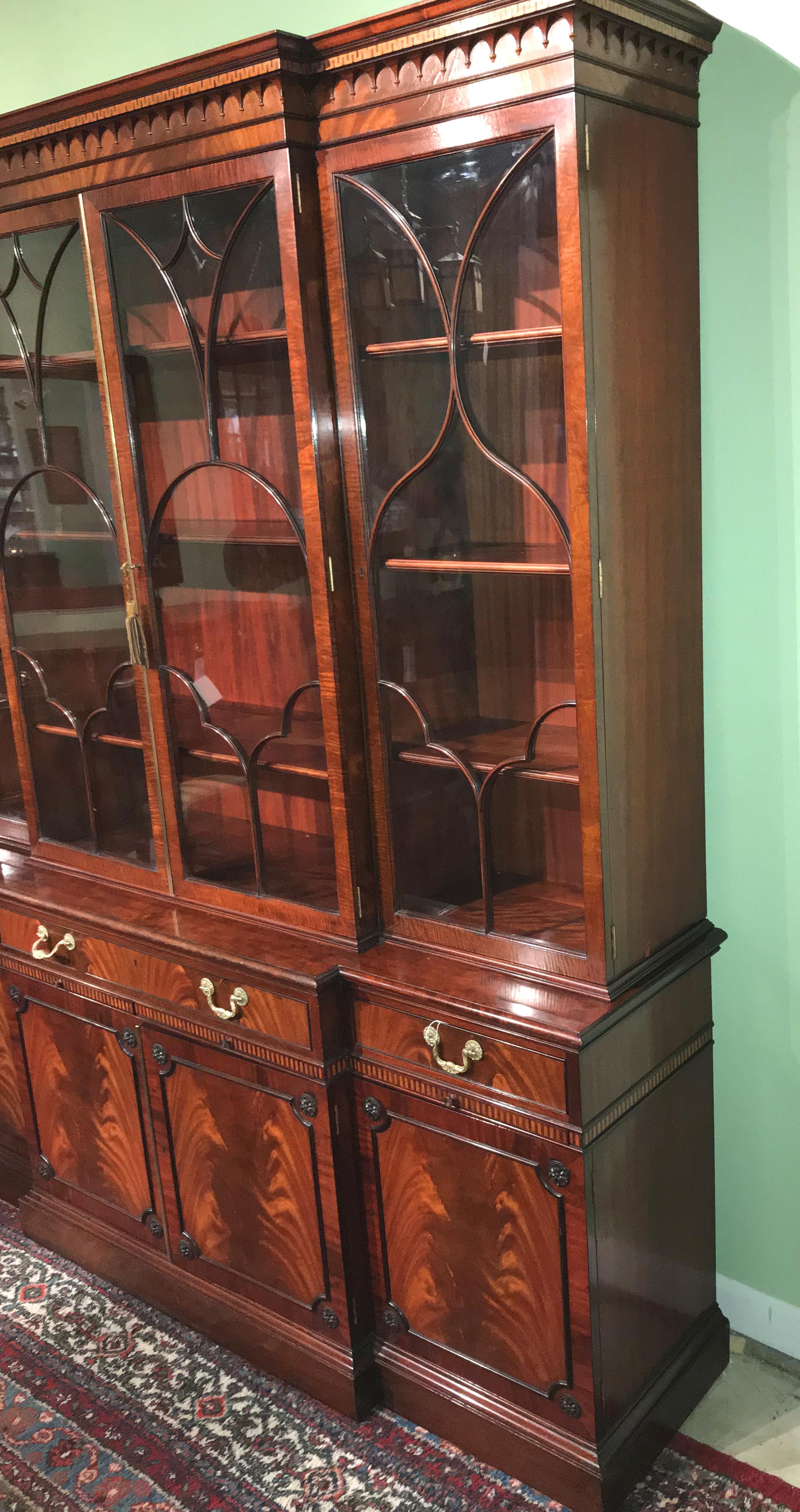 An elegant two part mahogany breakfront sideboard or china cabinet by Schmieg & Kotzian, its upper case with a decorative carved cornice with contrasting key inlay, surmounting four glazed glass doors which open to three adjustable shelves with