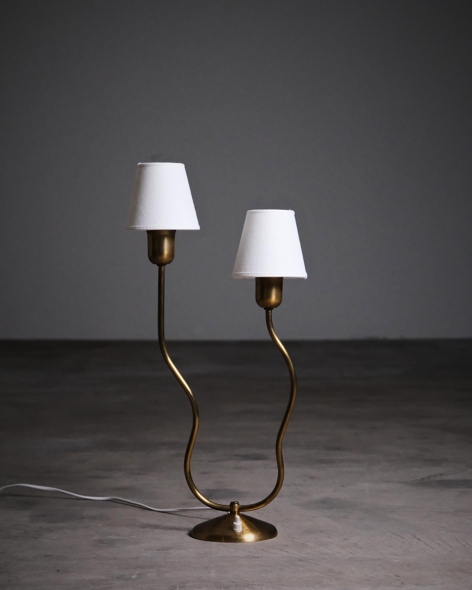 A Scandinavian Modern table lamp from the first half of the 20th century, designer and manufacturer unknown. Crafted in brass and metal, the piece stands out with its sculptural twin-arm design and graceful curves.

A refined and decorative lamp