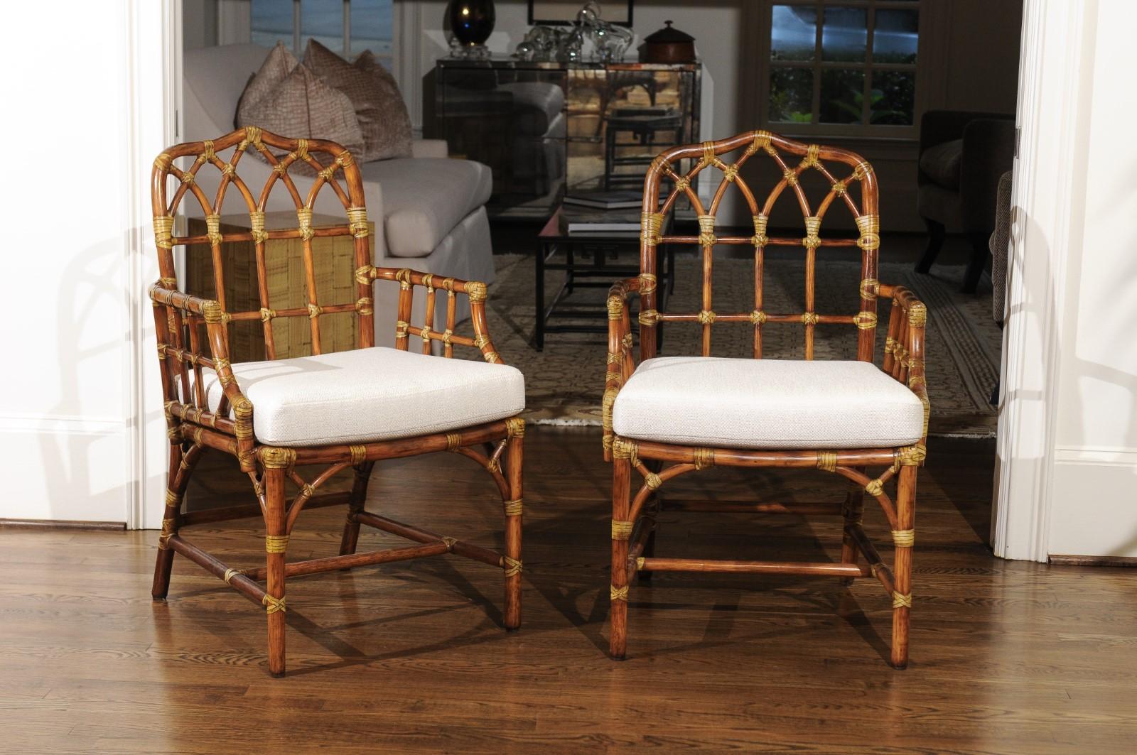 A radiant restored set of eight difficult to find arm dining chairs by McGuire, circa 1970. Stunning expertly crafted rattan and cane construction with an exquisite Cathedral back detail. Handsome accent bindings in the Maker's iconic trademark