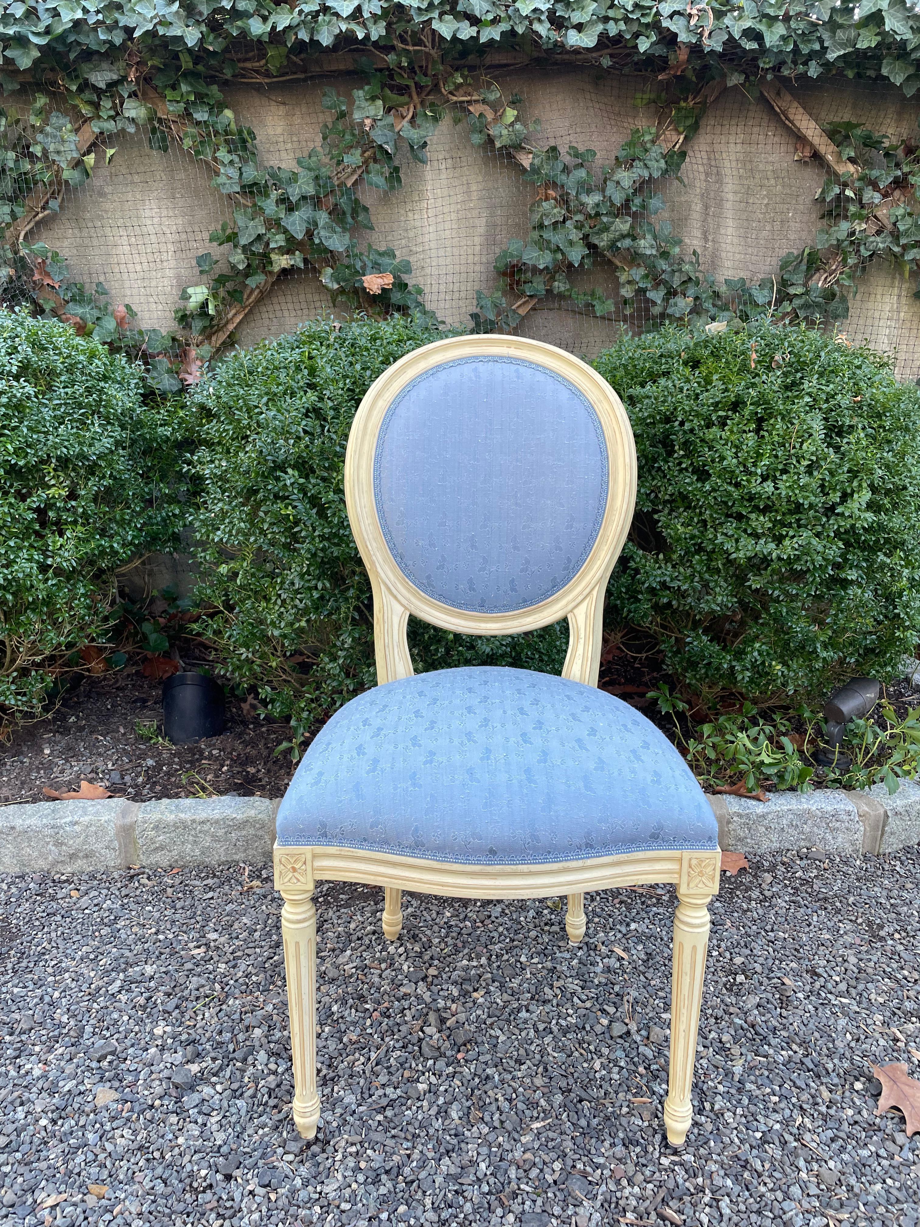 Lovely vintage set of eight Louis XVI style dining chairs painted in an off white. The set consists of five rectangular backs and three oval backs, each upholstered in a blue brocade. The backs of each chair are upholstered in a blue and white check