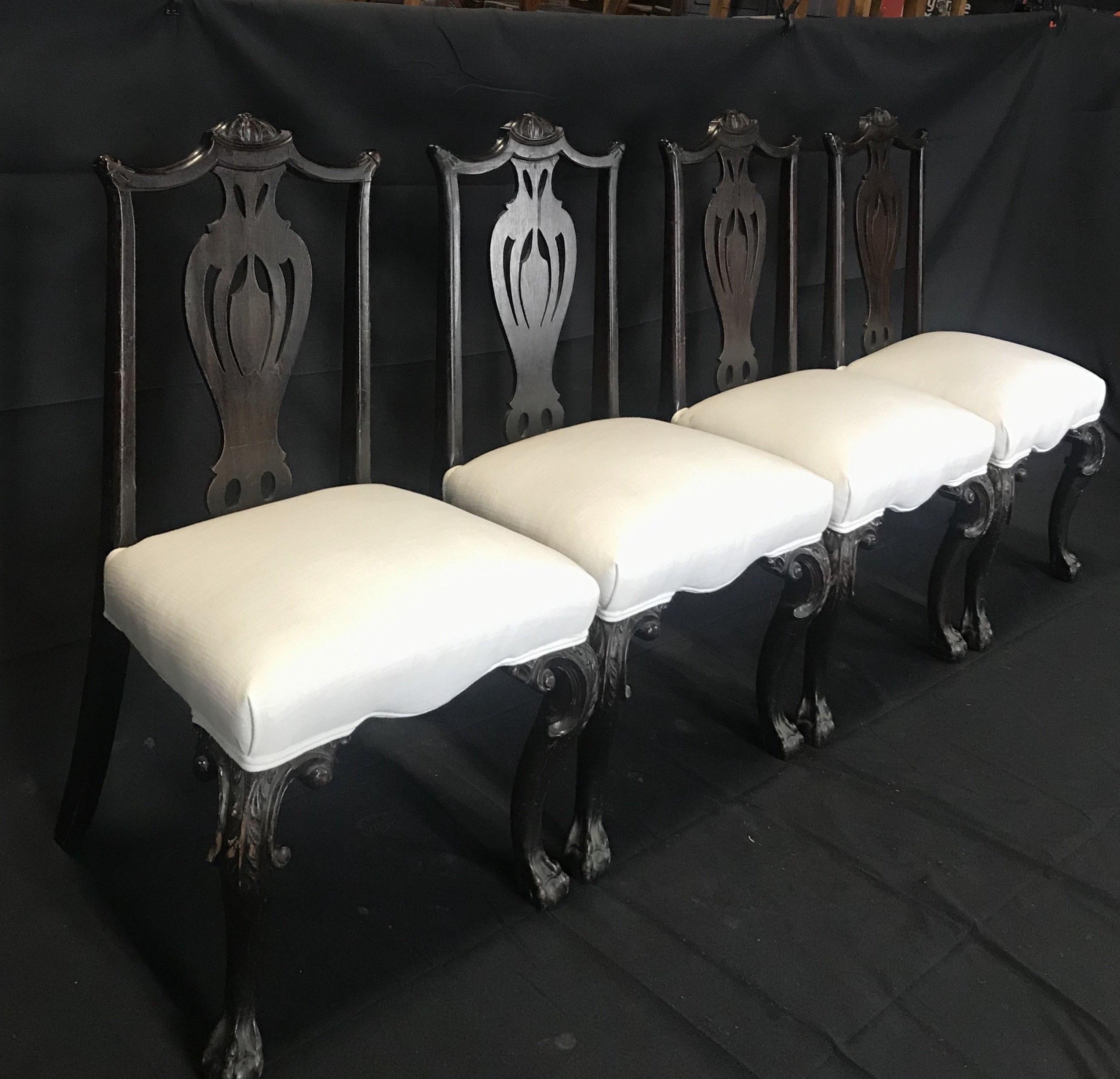 A beautiful set of four carved antique English Chippendale style mahogany dining chairs. Classic in style, newly upholstered, and the naturally dark wood has been magnificently detailed, designed and hand carved, including the ball and claw
