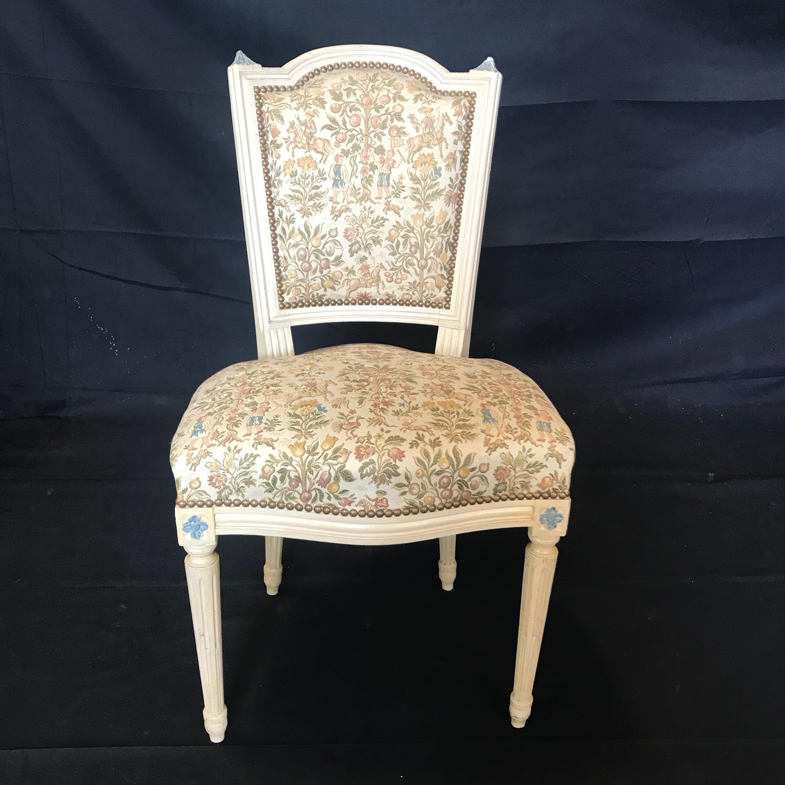 Gorgeous set of 6 antique Louis XVI dining chairs having original ivory paint and beautiful neutral tapestry upholstery in excellent shape with a beautiful tack border. Each of the chairs has a unique set of scenes on the tapestries: one for the