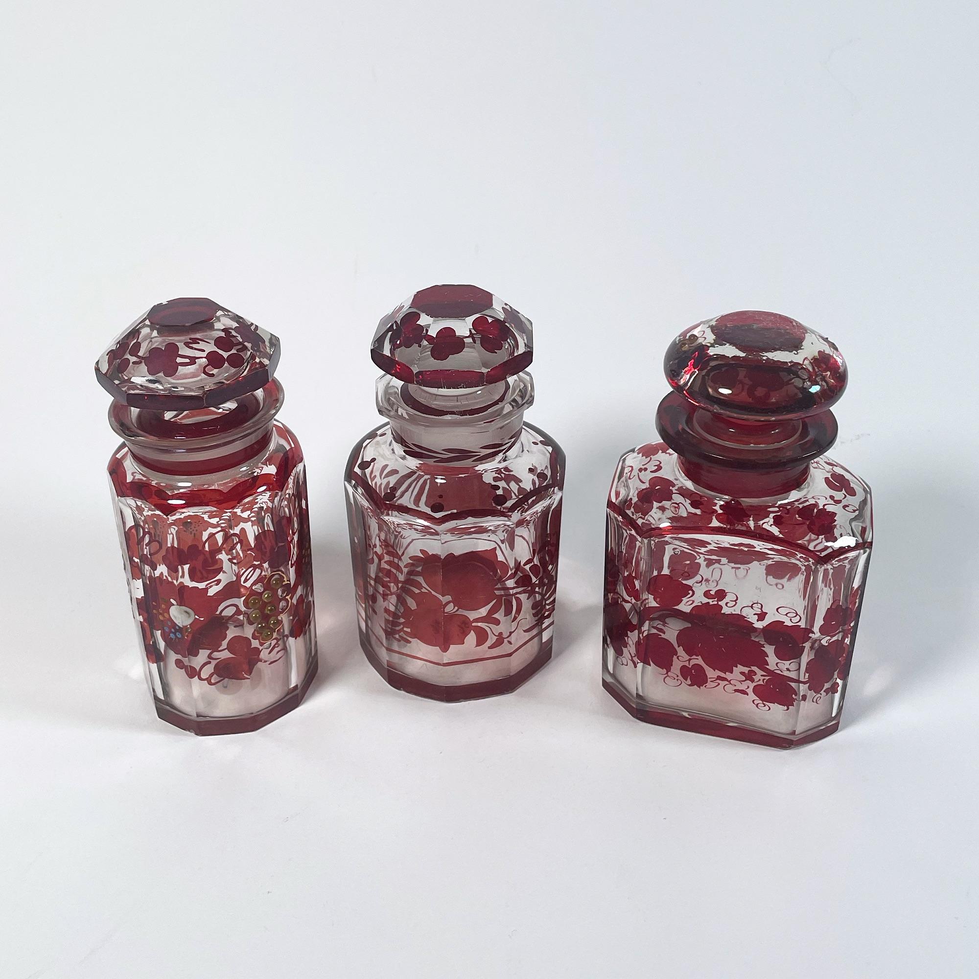 Discover the charm of this exquisite set of three red glass bottles, each a stunning example of 1940s Bohemian craftsmanship. The tallest bottle stands at 15.5 cm with a diameter of 6.5 cm, while the rectangular bottle measures 14.5 cm in height and