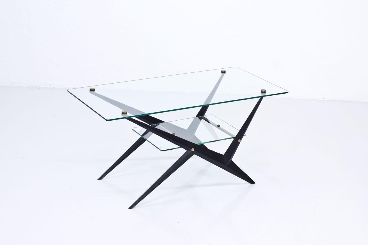 Coffee table designed by Angelo Ostuni. 
Manufactured in Italy during the 1950s. 
Glass top and lower tray, brass and black
lacquered metal frame / legs.