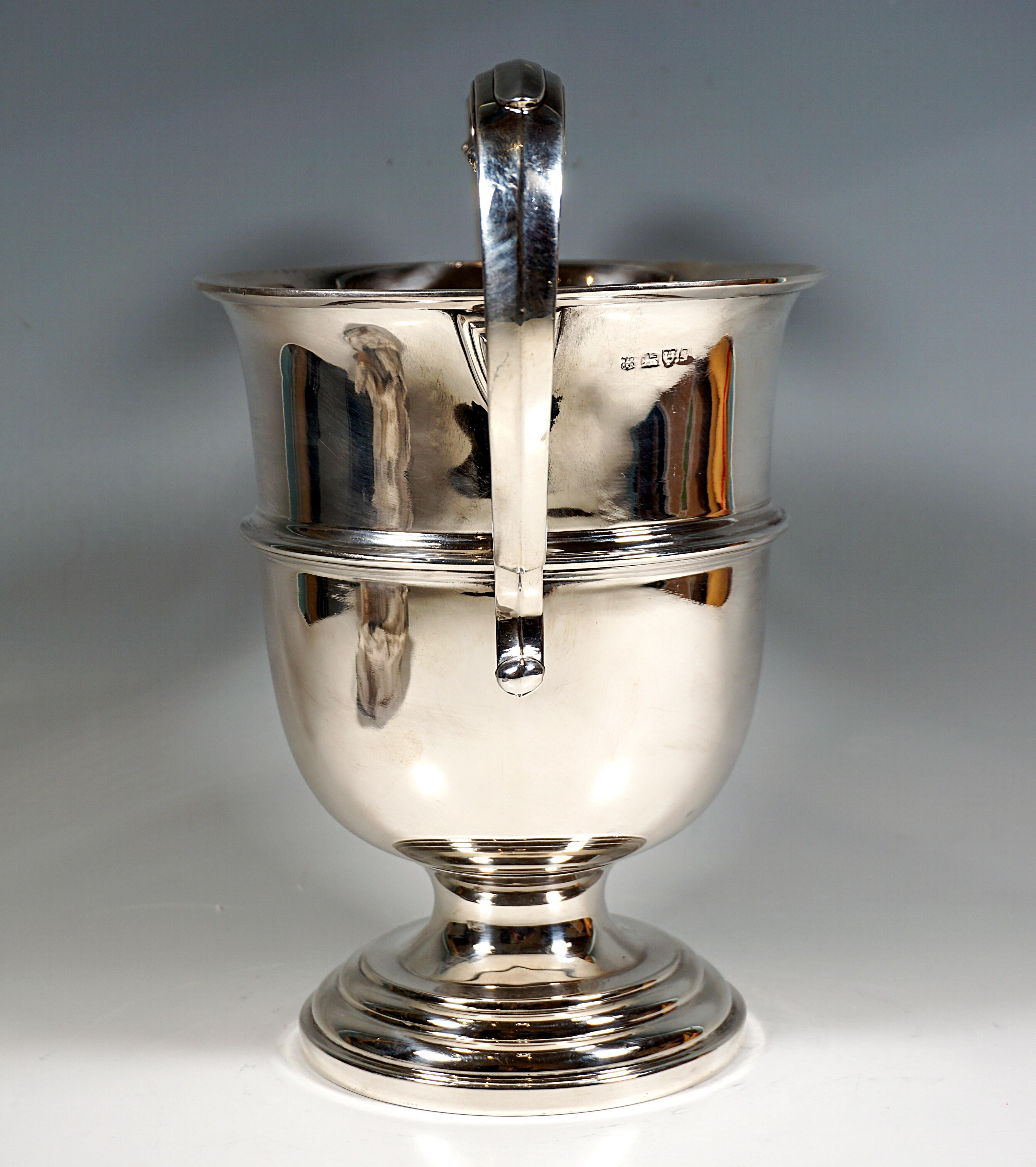Elegant crater-shaped silver wine cooler on an offset, stepped, round base with smooth, profiled walls and two large, raised volute-shaped handles.

925 Silver

Hallmarks:
Master's sign 'MEB FEB'- Barker Brothers, registered 1906
Coat of arms