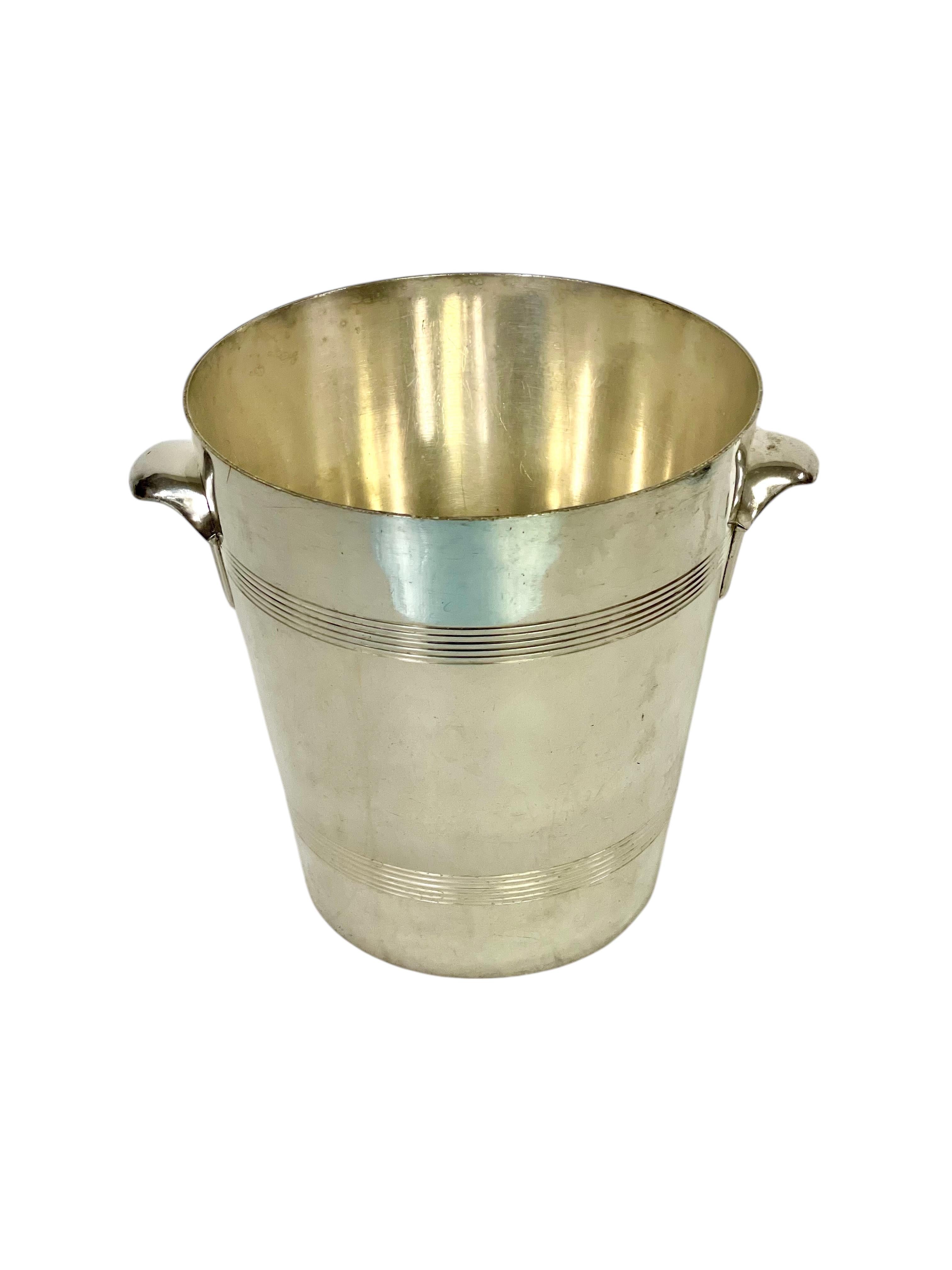 Se trata de un clásico cubo de champán plateado, que destila elegancia y refinamiento atemporales. Su forma cilíndrica, elegante y afilada, se realza con delicadas nervaduras horizontales, que añaden un elemento decorativo sutil pero sofisticado. La