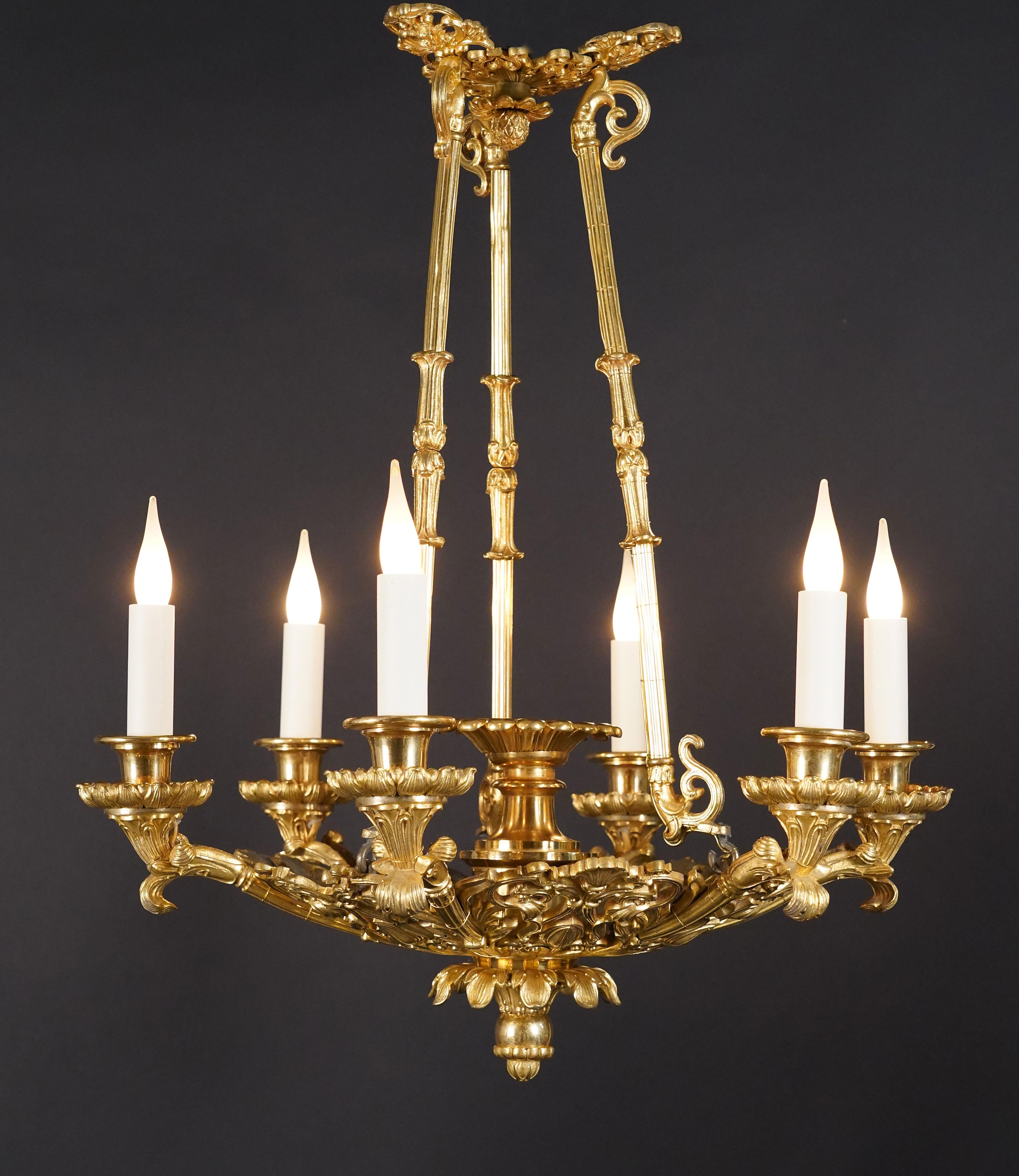 Elegant Louis-Philippe period chandelier in chased and gilded mercury bronze. The central part is composed of an openwork decor of foliate scrolls and shells from which six arms of light emerge, the whole supported by three uprights ending in a