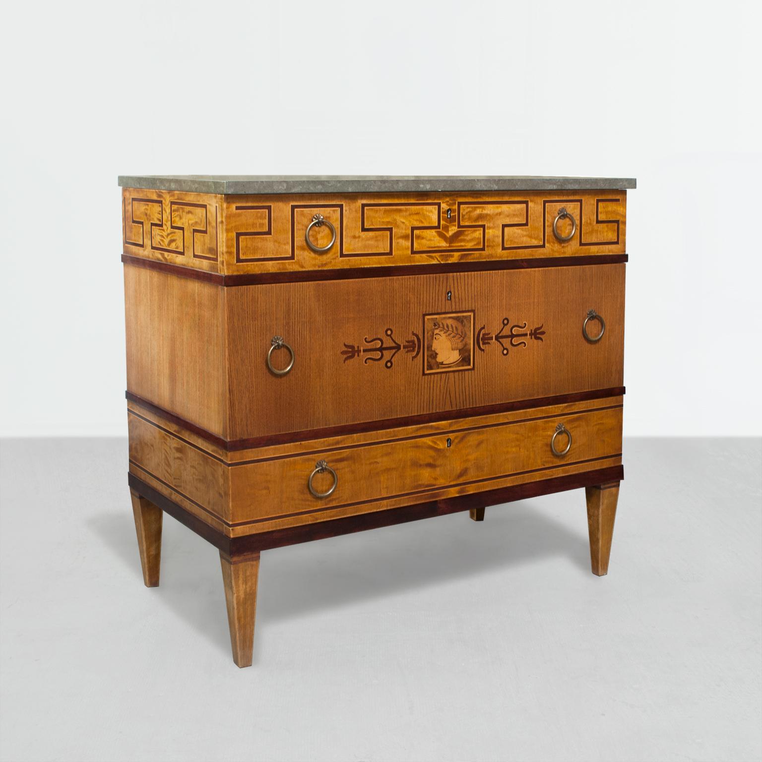 An elegant Swedish Art Deco 3-drawer marquetry chest of drawers with limestone top. The chest's upper section is detailed with a stylized meander design which wraps to the sides. The center drawer references classicism with a man's profile framed by