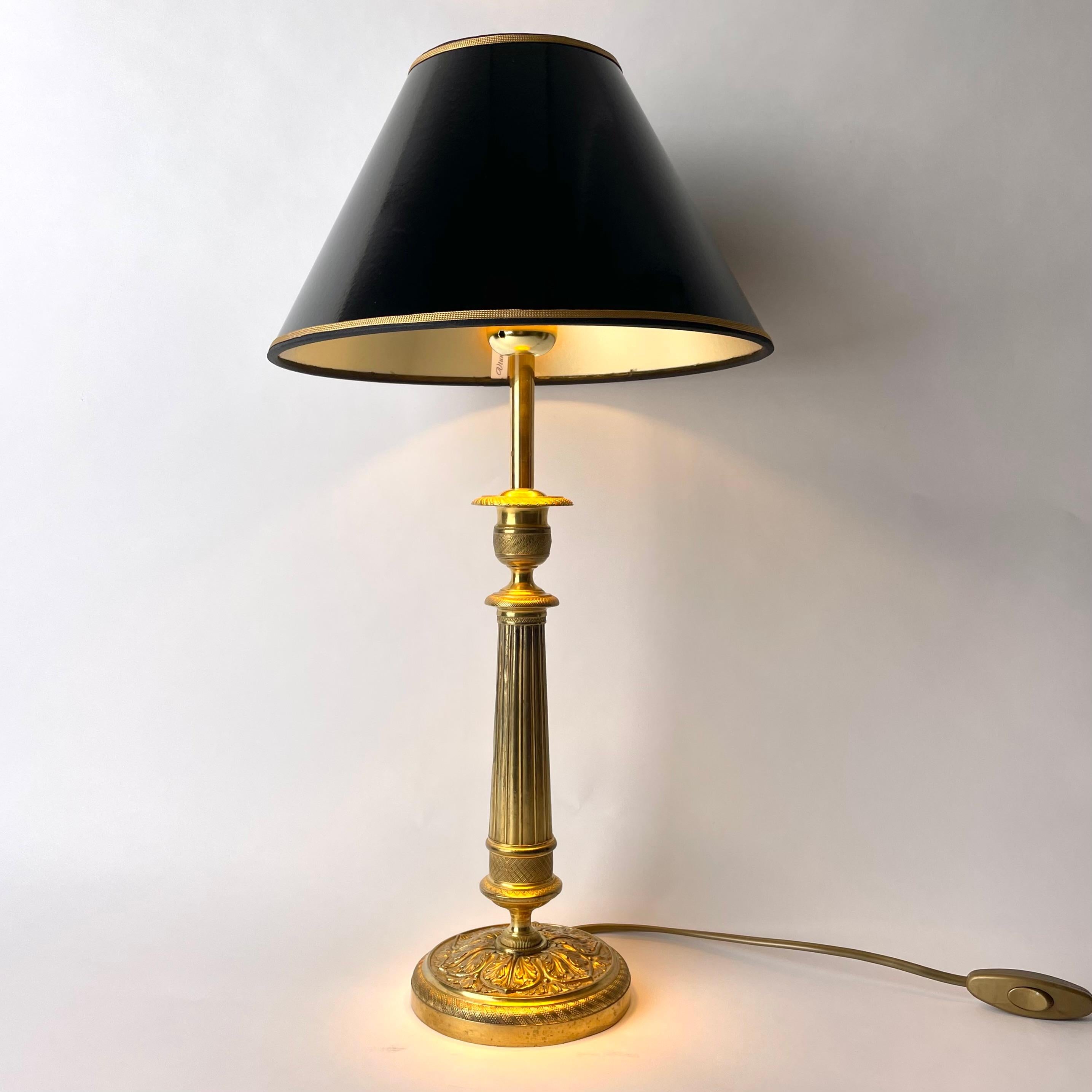 Elegant Table Lamp in bronze. Originally an Empire candlestick from France made during the 1820s. The middle part in the form of a column. Richly decorated with leaf and period Empire decorations.

New lampshade in black lacquer with a gilded inside