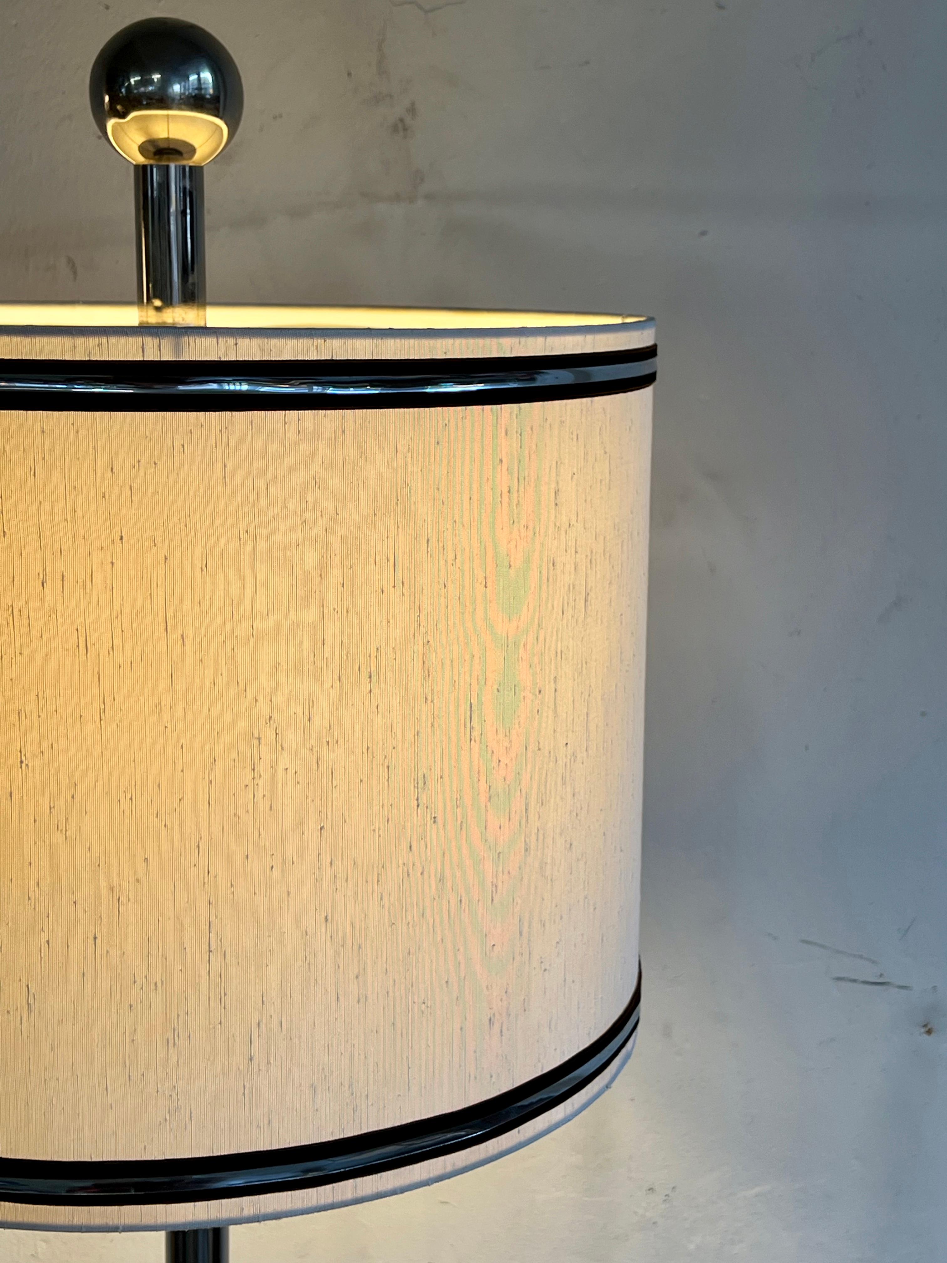 Grande lampe de table des années 60 à l'allure élégante. Probablement de fabrication allemande.
 
L'abat-jour en soie d'origine repose sur une solide base chromée et est orné d'une bande chromée. Au-dessus de l'abat-jour se trouve un diffuseur en