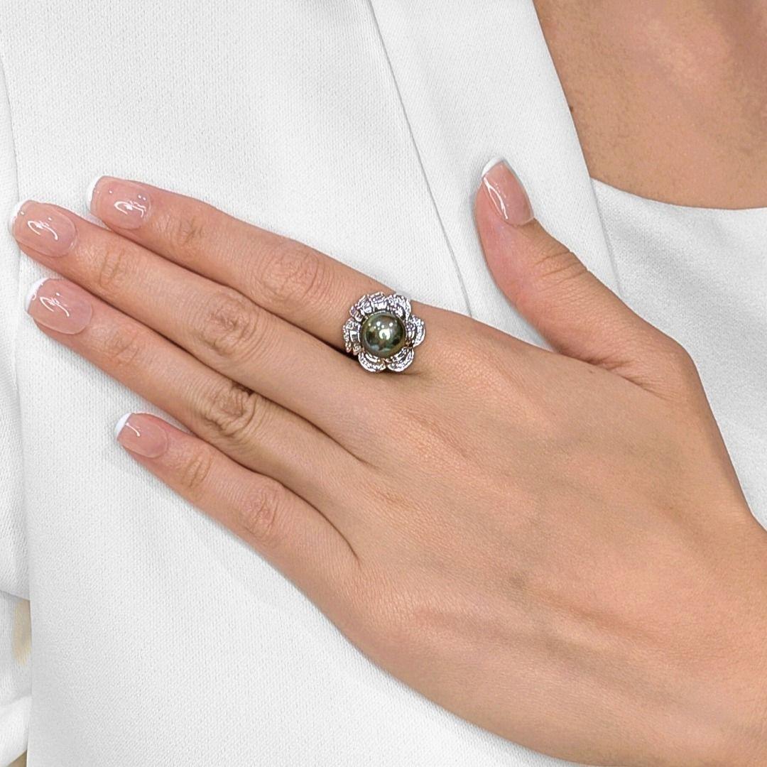 Dieser elegante Ring präsentiert eine leuchtende 10,3 mm große Tahiti-Perle in einem bezaubernden Grün-Grau-Ton, eingebettet in eine floral inspirierte Fassung aus 18 Karat Weißgold. Die Perle ist von 40 natürlichen Diamanten umgeben - 20 runde