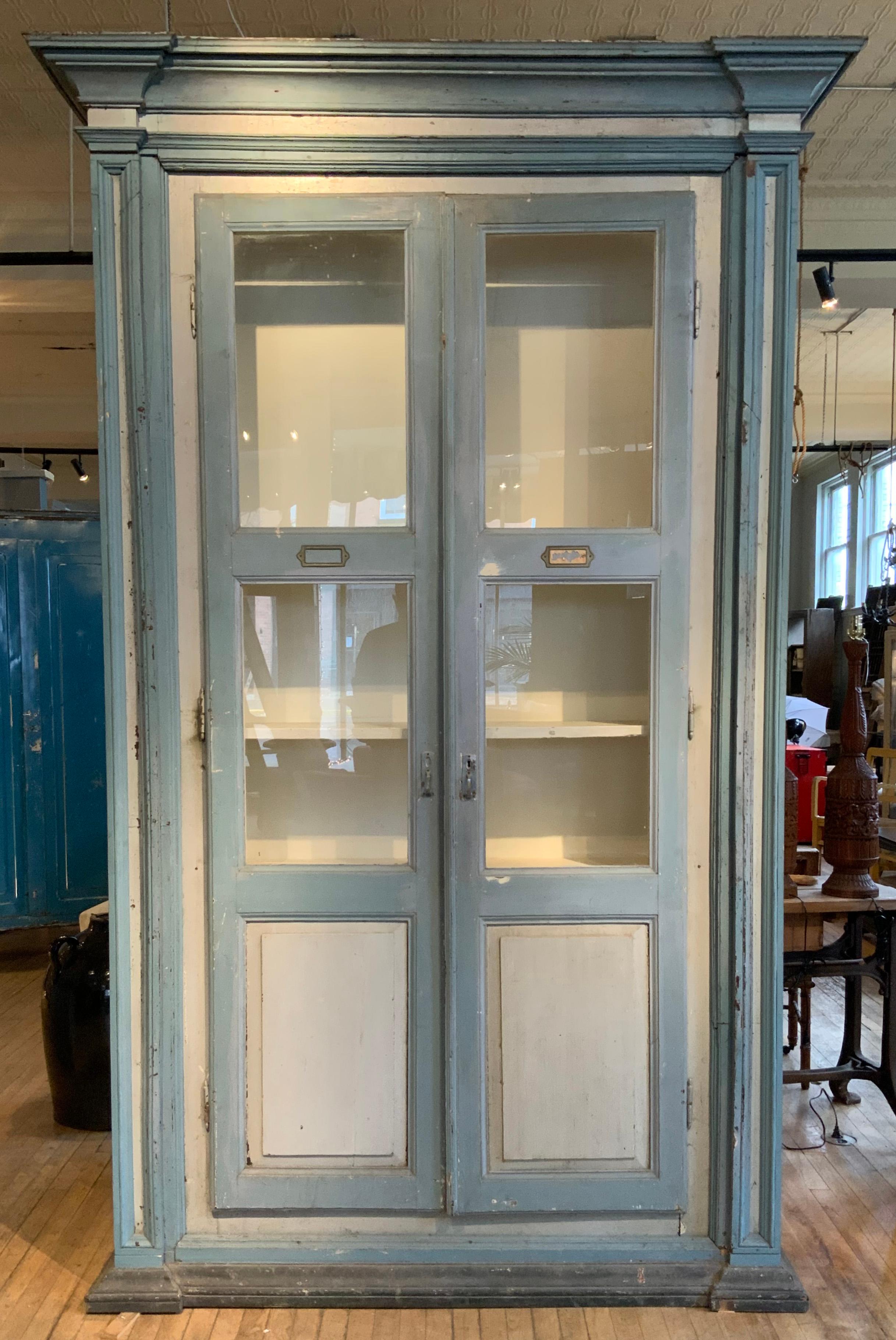 a beautiful antique 19th century Italian tall painted cabinet, with exaggerated stepped molding capital, and a pair of antique glass doors. lovely painted finish in cream and powder blue, with panelled details on the sides and front of the cabinet.