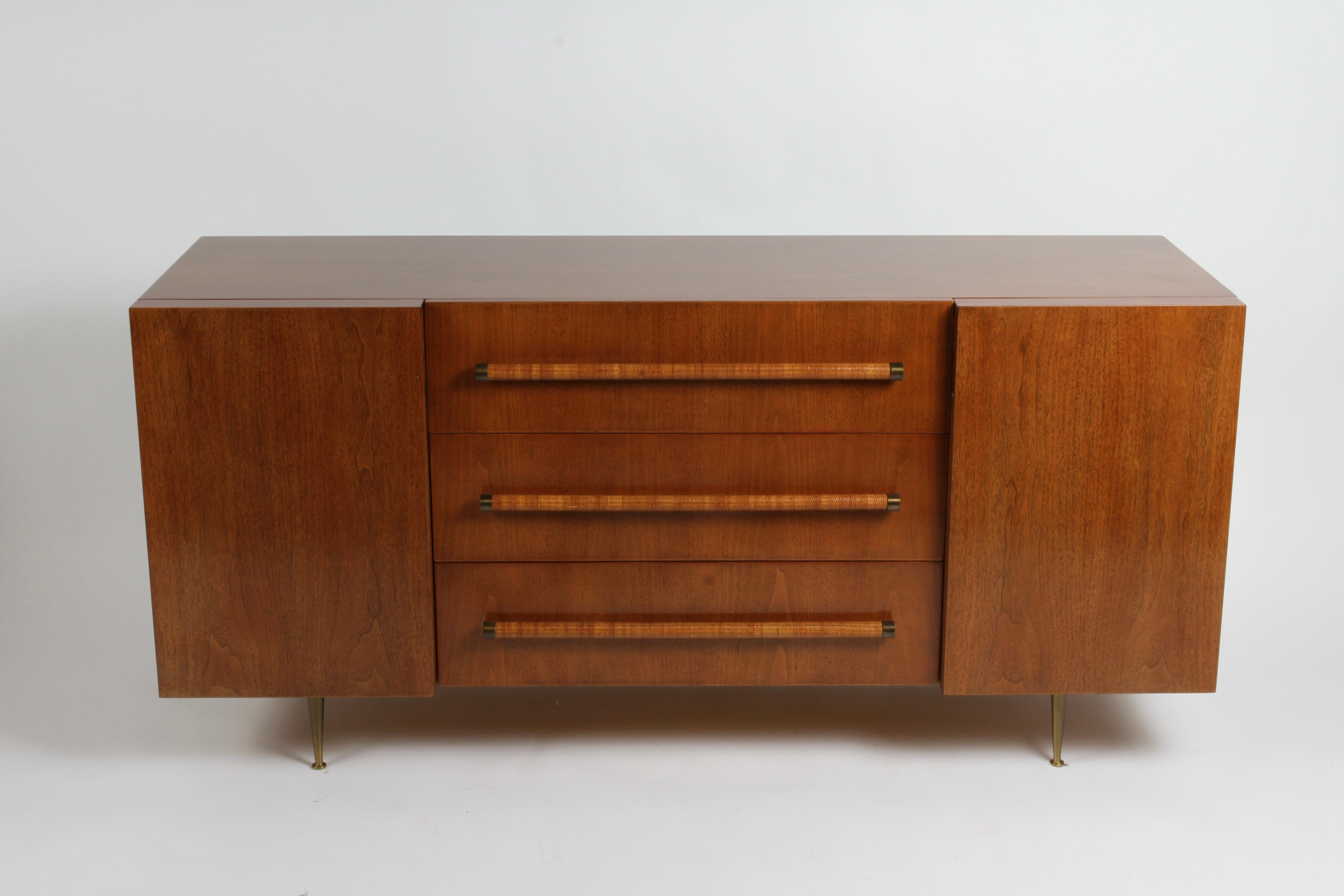 Rarely seen elegant T.H. Robsjohn-Gibbings for Widdicomb sideboard or dresser. Completely restored cabinet to original color shown. Walnut cabinet with center drawers with rattan circular handles with brass end caps, two end cabinets with shelves on