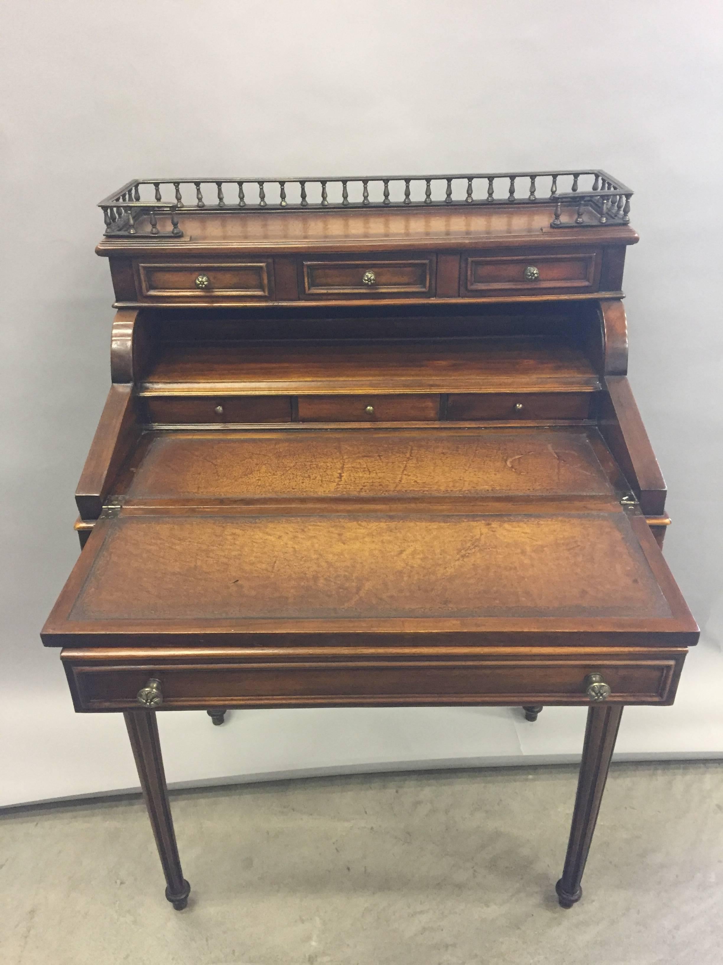 Refined traditional English style flip front desk having a gallery top over roll top centre with fold over desk surface. The writing surface is yummy cognac leather. Elegant fluted legs and handsome brass gallery and hardware.