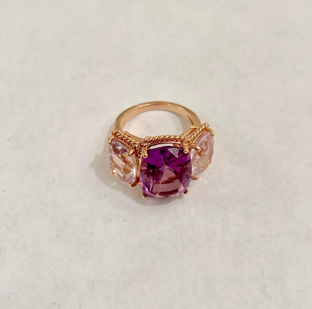 Elegant 18kt Rose Gold Three Stone Ring with Rope Twist Border with split shank detail. The ring features a faceted cushion cut Deep Amethyst Center stone and two Pale cushion cut Amethyst side stones stones surrounded by twisted gold rope. The